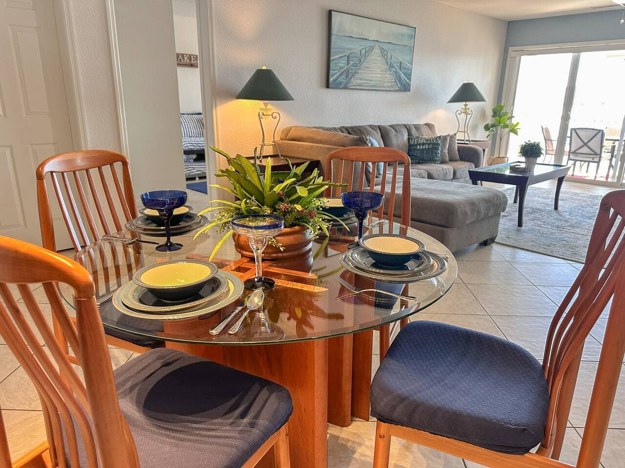 A bright, open-concept living and dining area featuring a cozy sectional, glass dining table, and sliding doors leading to the lakefront deck. Natural light fills the space, creating a relaxing environment.
