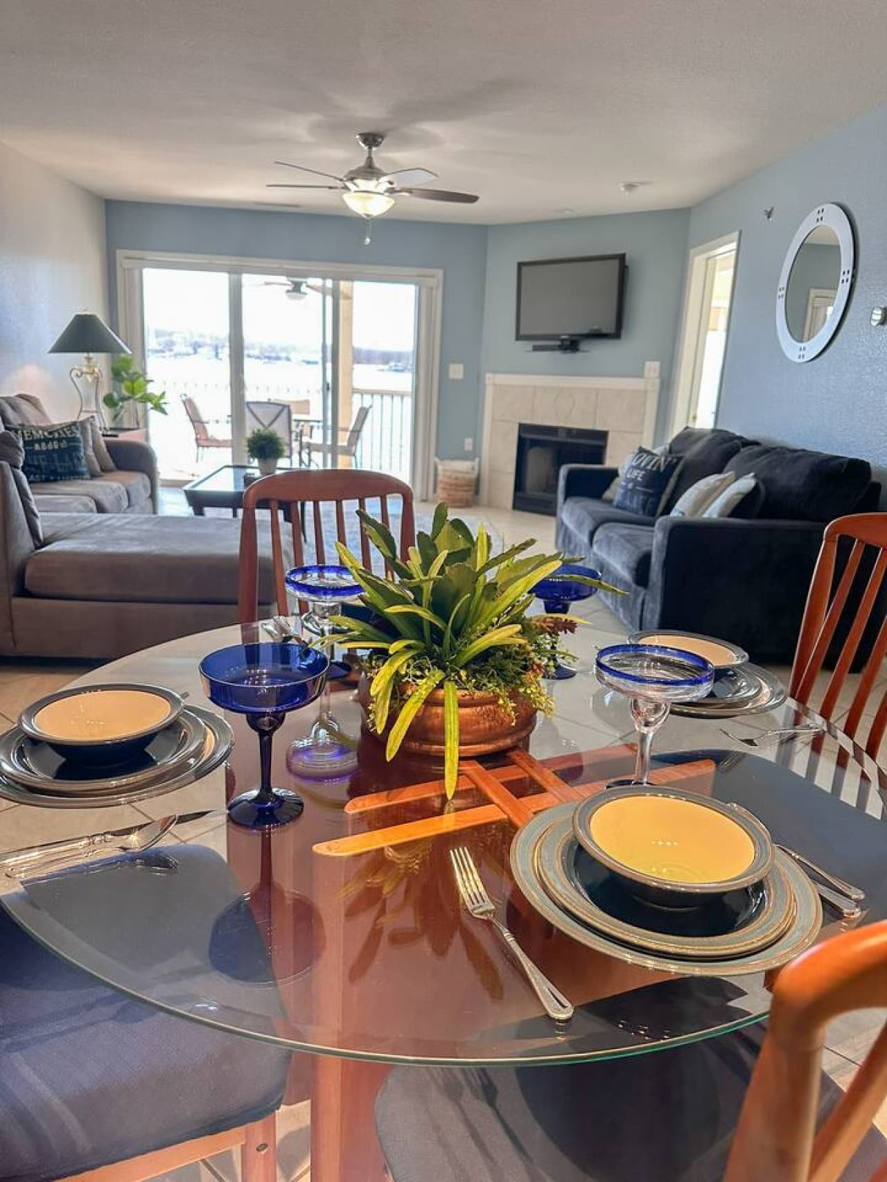 A cozy and stylish dining space with a view of the inviting living room, featuring a mounted TV, fireplace, and a large window showcasing the stunning lake scenery.