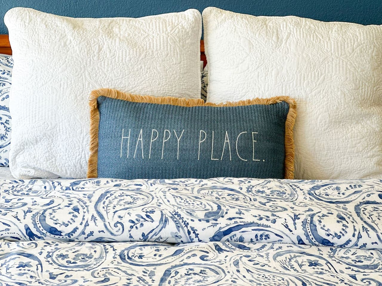 A beautifully styled bed with soft, inviting textures and a charming "Happy Place" pillow—perfect for unwinding.