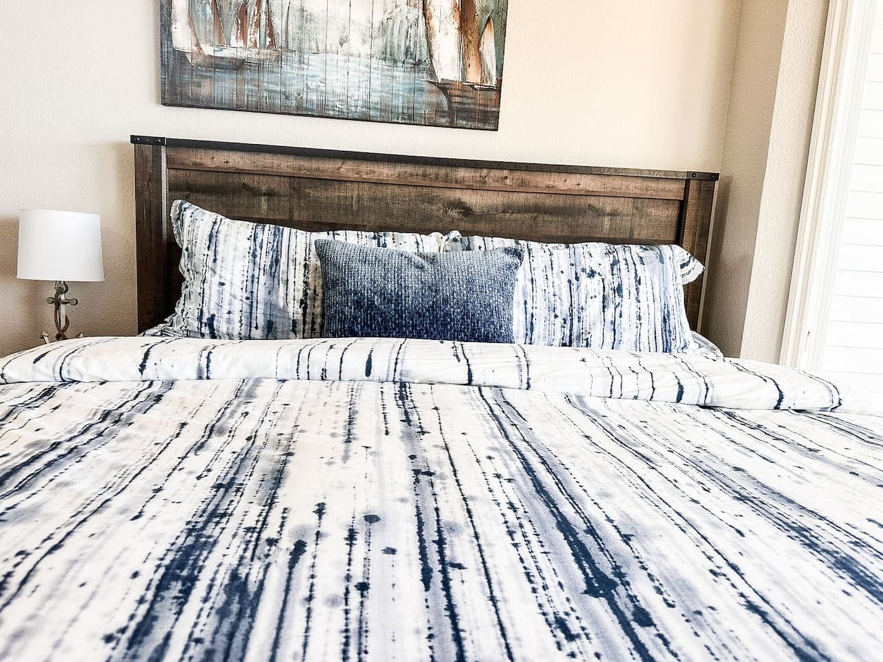 A serene space with a wooden headboard, coastal-inspired bedding, and soft lighting, creating a comfortable and restful atmosphere.