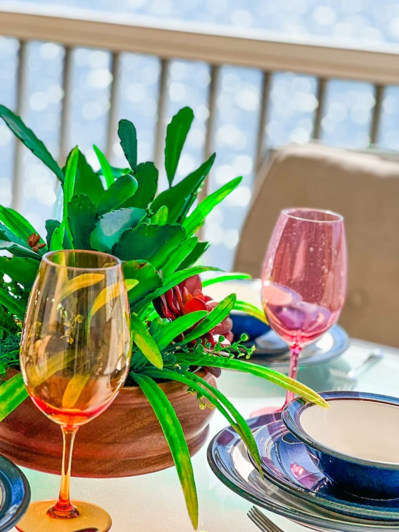 A beautifully set table on the patio, featuring colorful glassware and lush greenery, perfect for a lakeside meal.