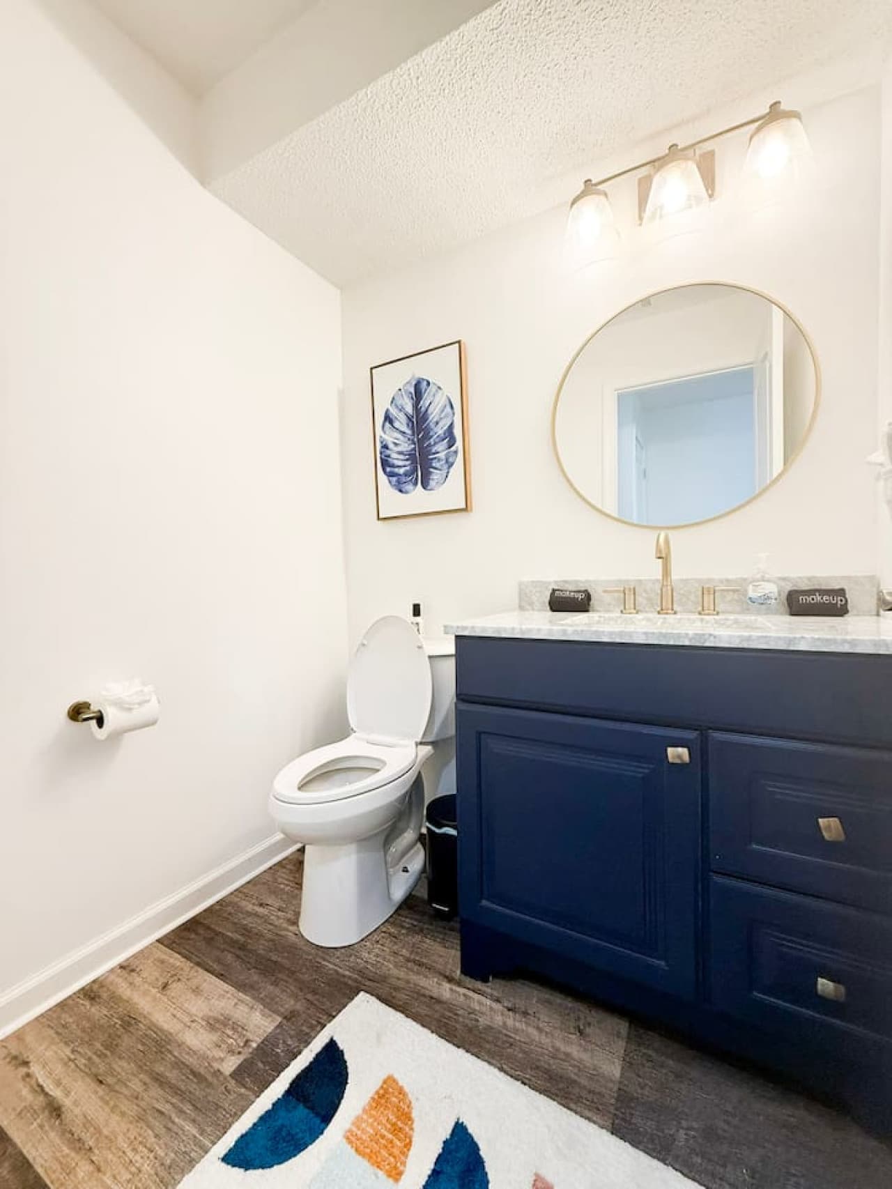 Modern bathroom with navy vanity and bright lighting.