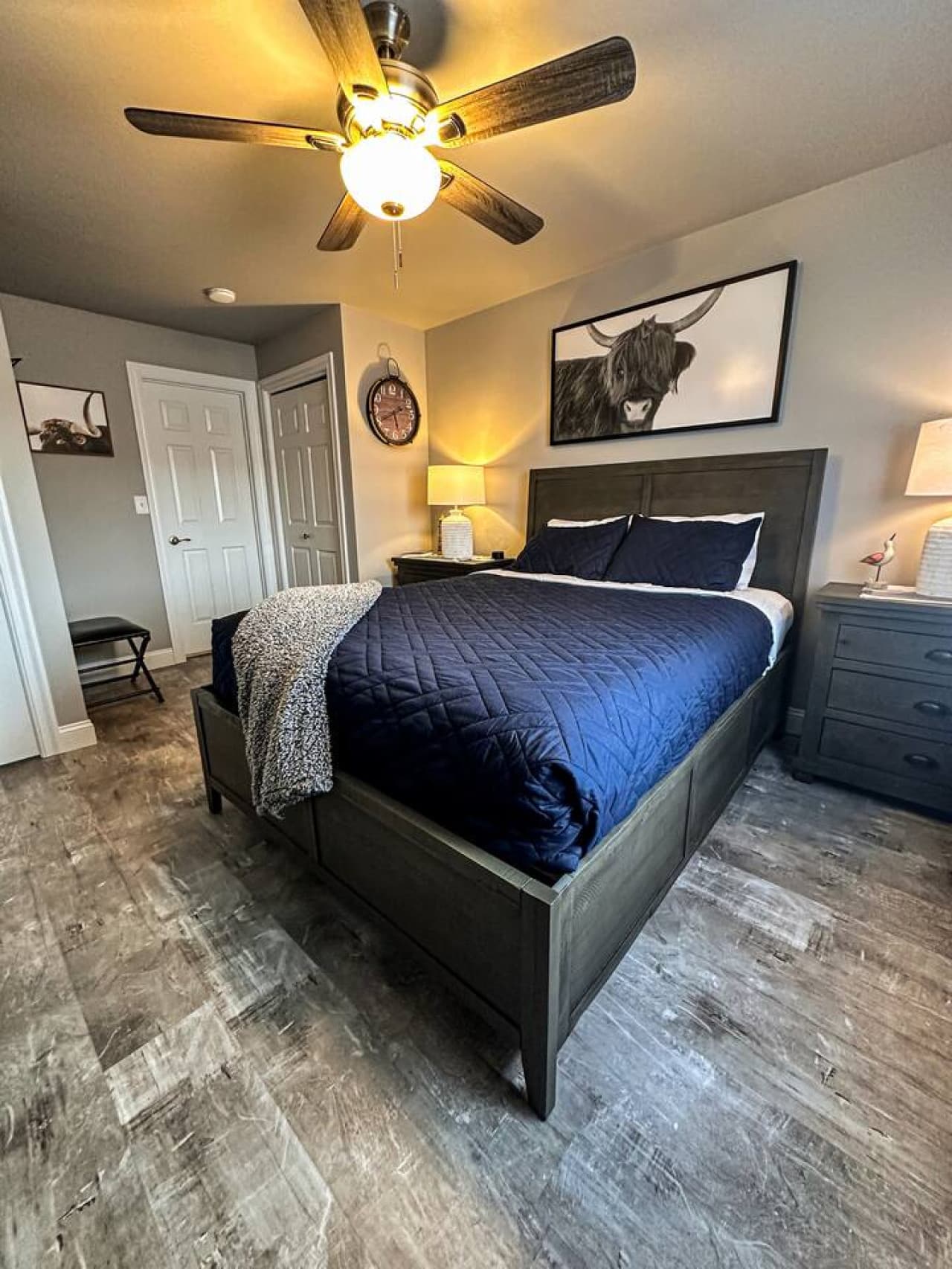 The bedroom features soft lighting, modern furniture, and rustic artwork for a tranquil stay.