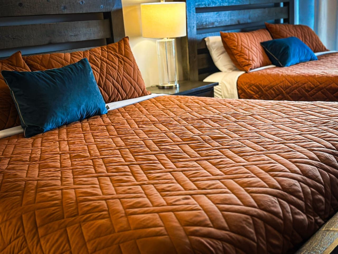 Close-up of the luxurious king-size beds, showcasing the elegant orange quilted bedding and soft accent pillows for ultimate comfort.