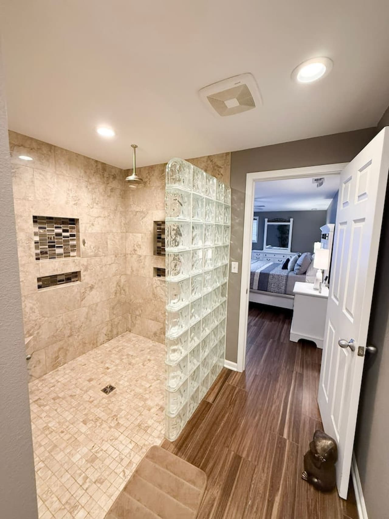 Spacious walk-in tile shower leading to a cozy bedroom.