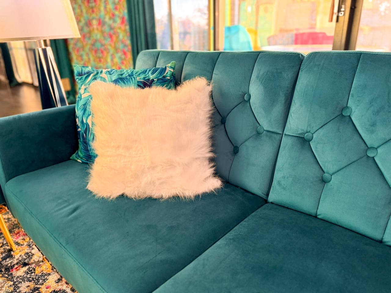 Detail of a stylish, tufted teal sofa with decorative pillows.