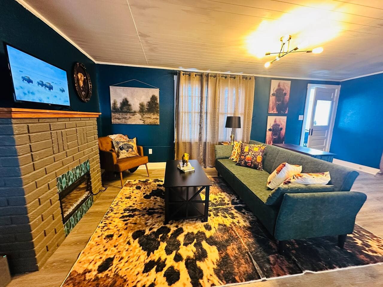 A cozy Western-inspired living room featuring bold navy walls, a rustic brick fireplace, and cowhide-patterned accents for a touch of cowboy charm.
