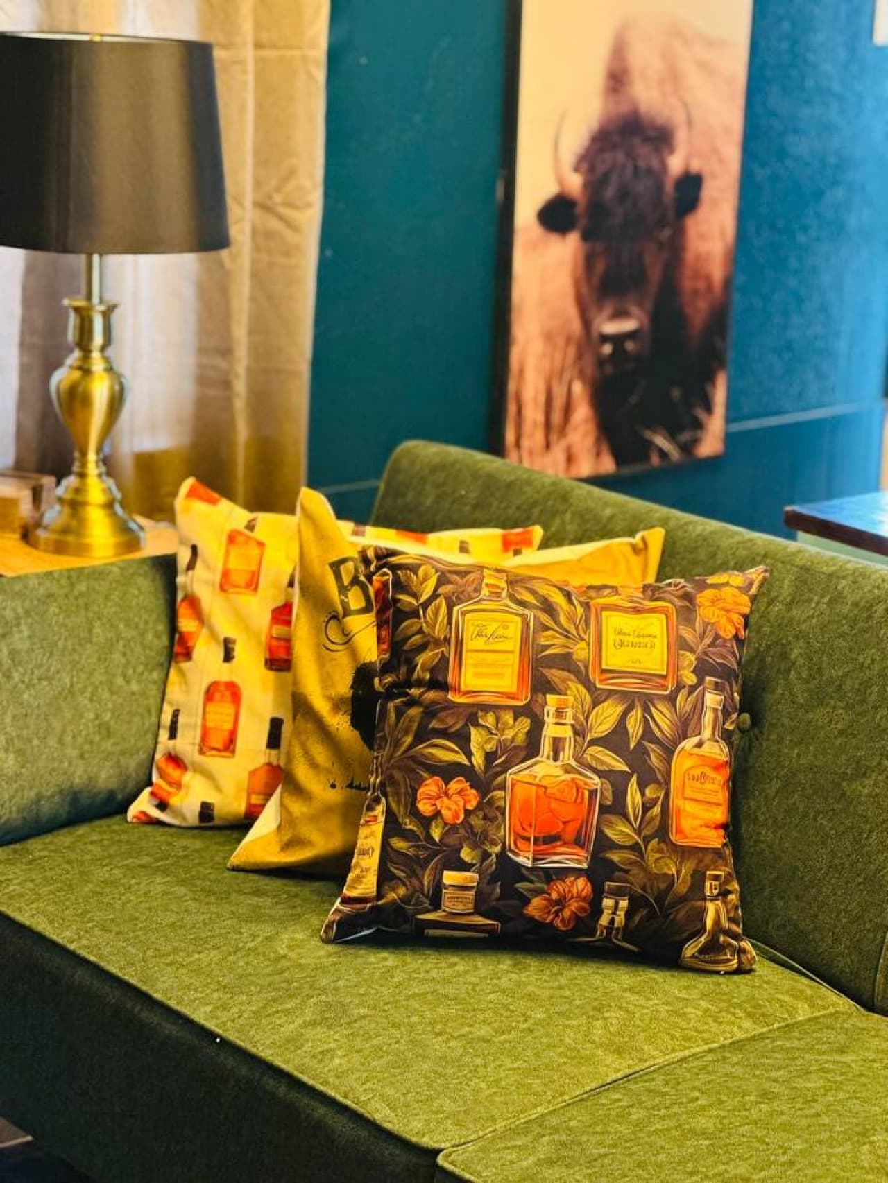 Signature bourbon-themed pillows add playful flair to this forest green couch, blending masculine style with cozy textures.