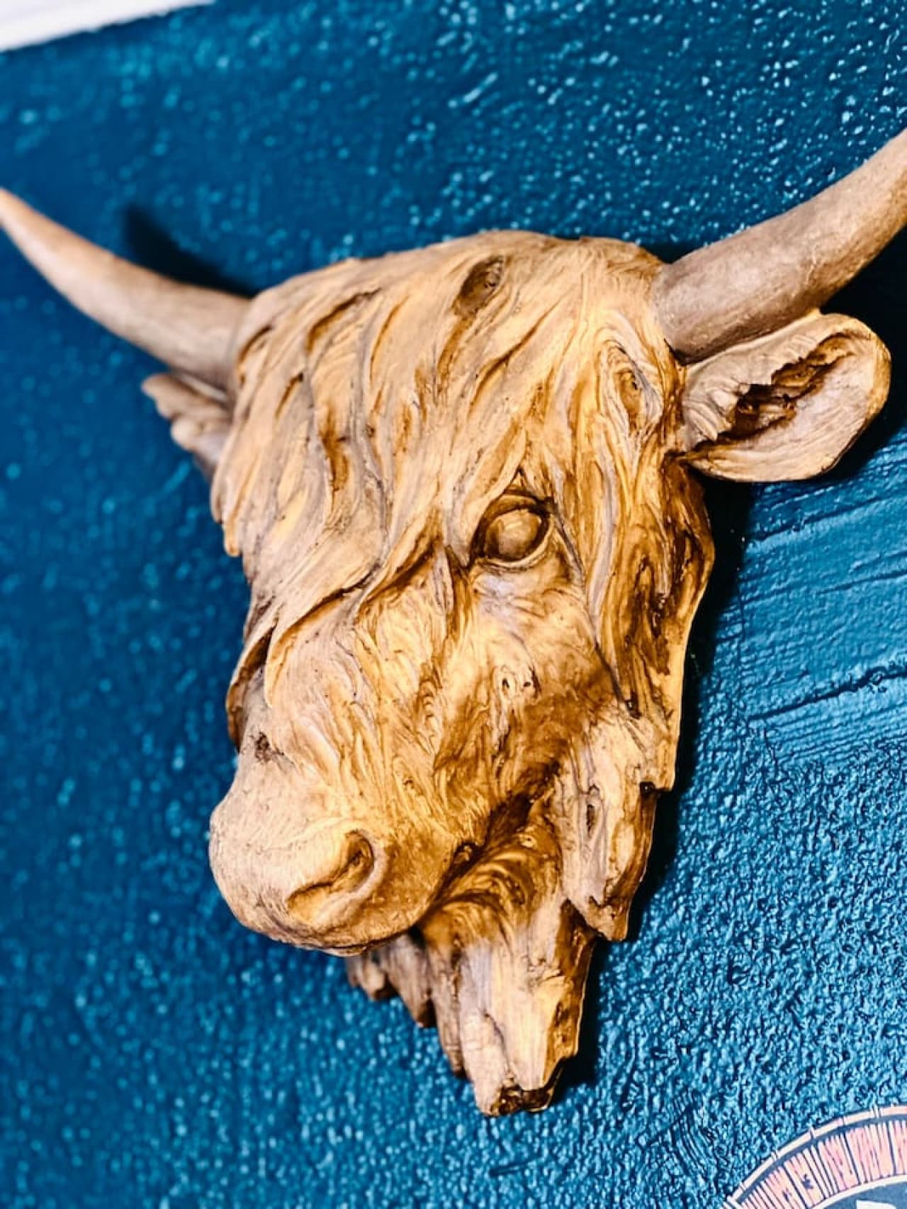 This close-up showcases a rustic, sculpted head of a Highland cow mounted on a deep teal wall, adding a touch of Western charm and unique character to the space. The textured details of the sculpture bring a tactile element to the decor, creating a f