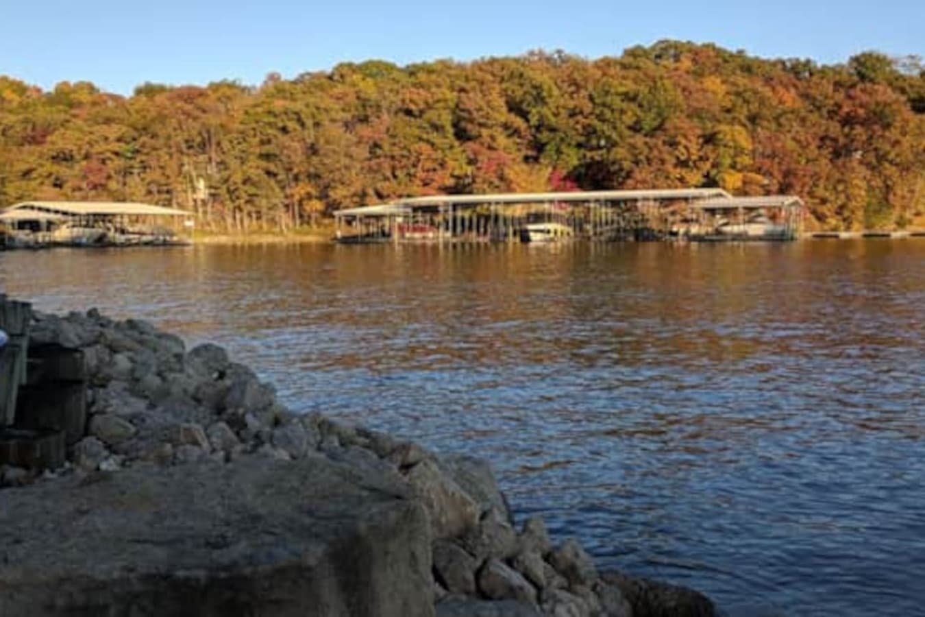 This expansive aerial view showcases the stunning Lake of the Ozarks, surrounded by vibrant fall foliage, offering a truly picturesque setting. The property boasts multiple boat docks, providing convenient access to the water for all your aquatic adv