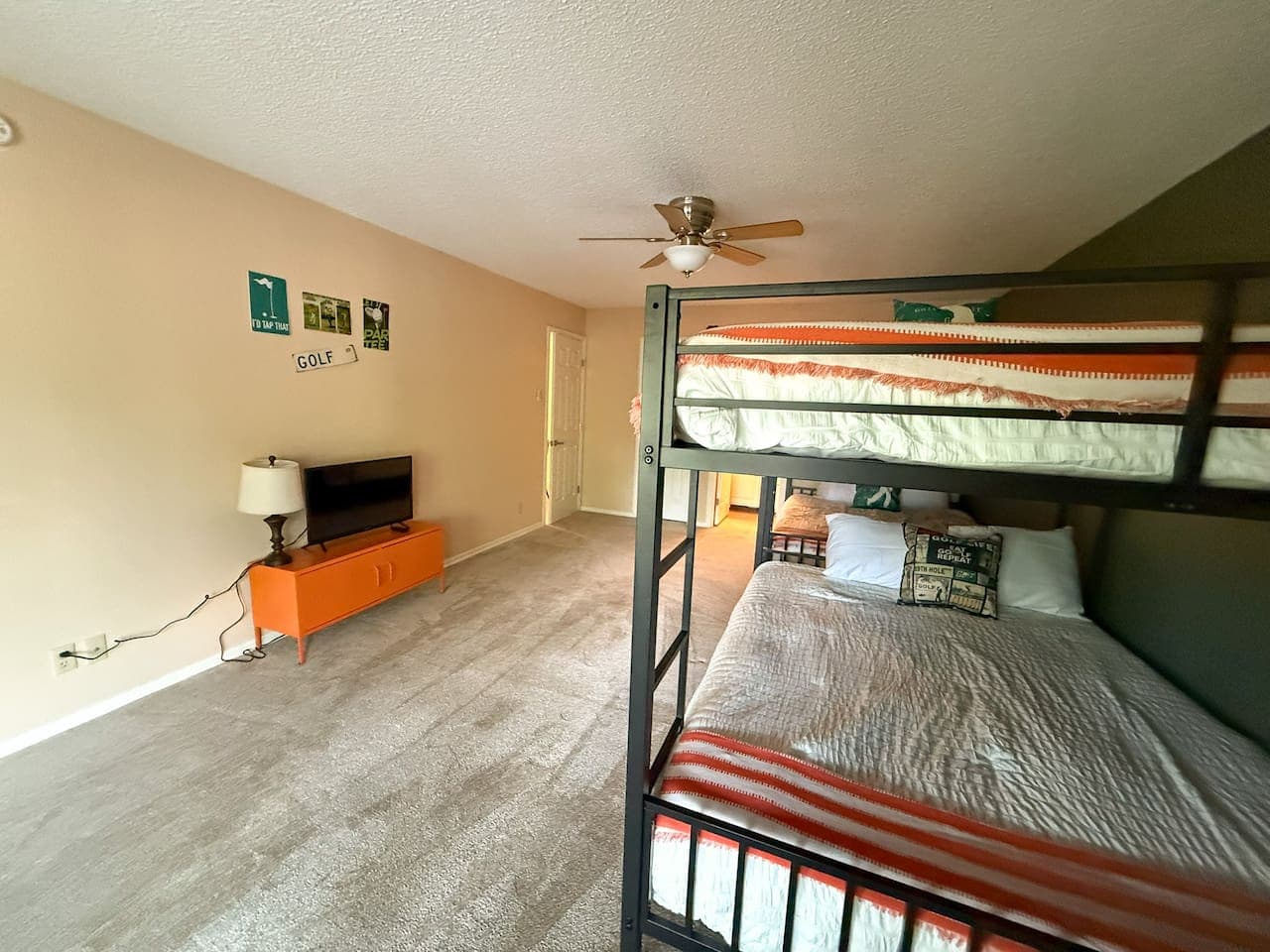This spacious room features two sturdy black metal bunk beds, offering ample sleeping arrangements perfect for guests or a large family. A neutral carpet and a striking dark green accent wall complement the functional design, while a ceiling fan ensu