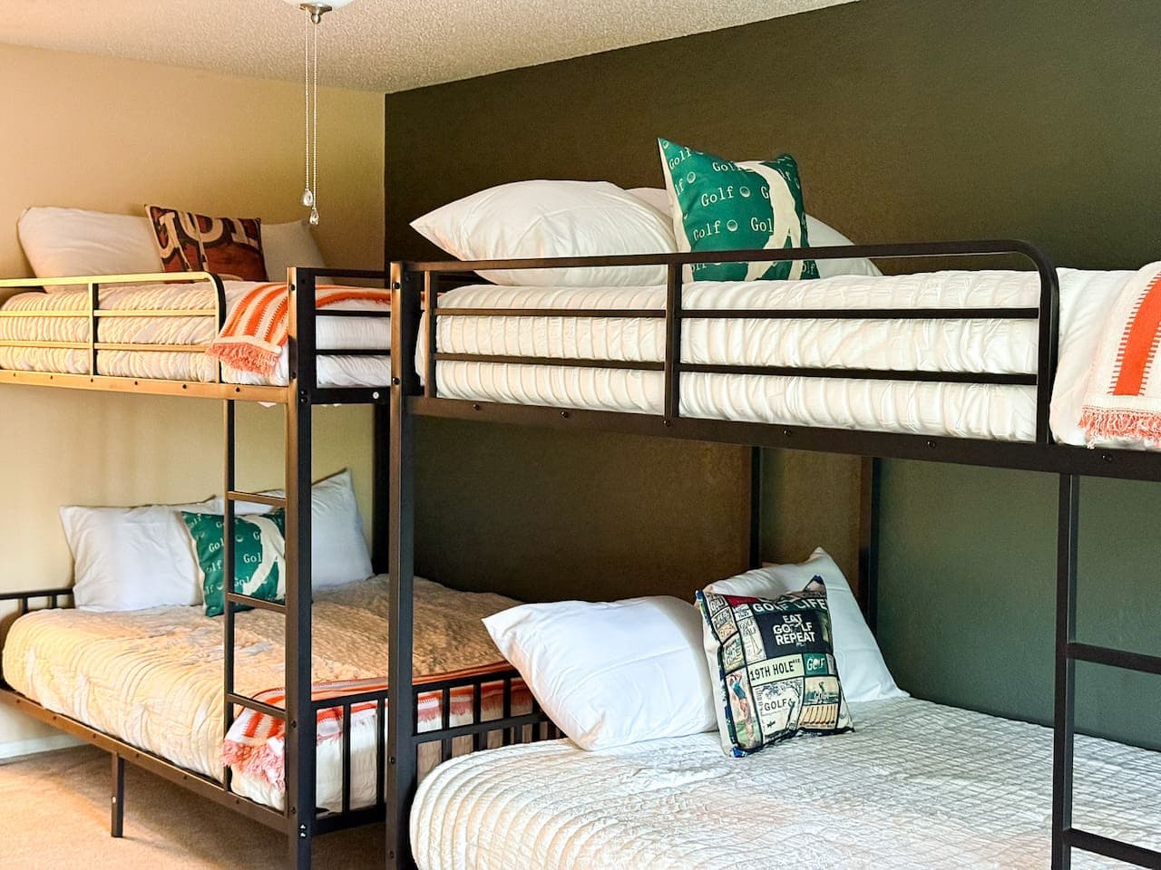 This inviting room features two sets of black metal bunk beds, perfect for accommodating a large family or group of guests. The unique olive green accent wall and golf-themed decor add a touch of personality and charm to this functional space.