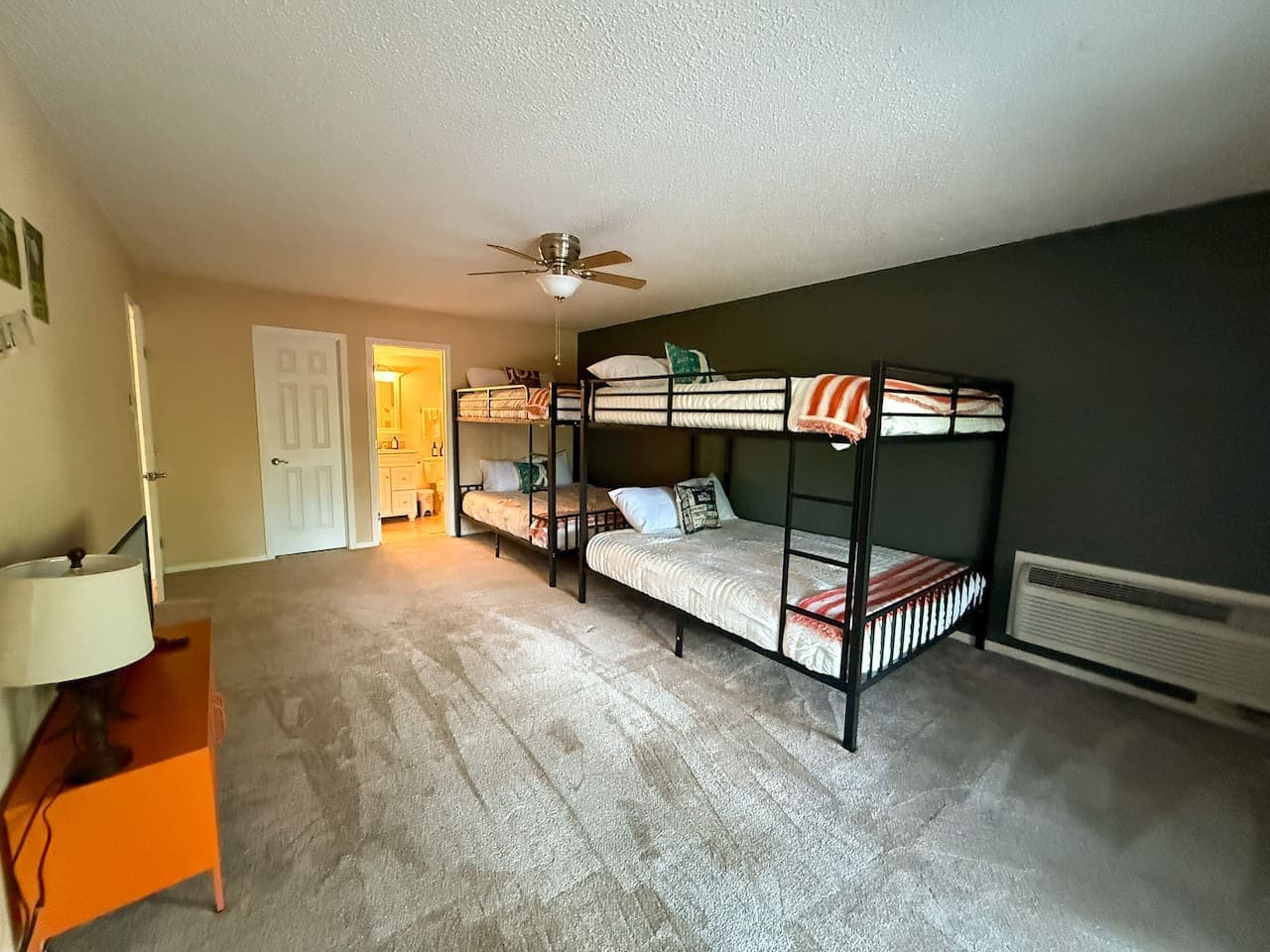 This inviting room features two sets of black metal bunk beds, perfect for accommodating a large family or group of guests. The unique olive green accent wall and golf-themed decor add a touch of personality and charm to this functional space.