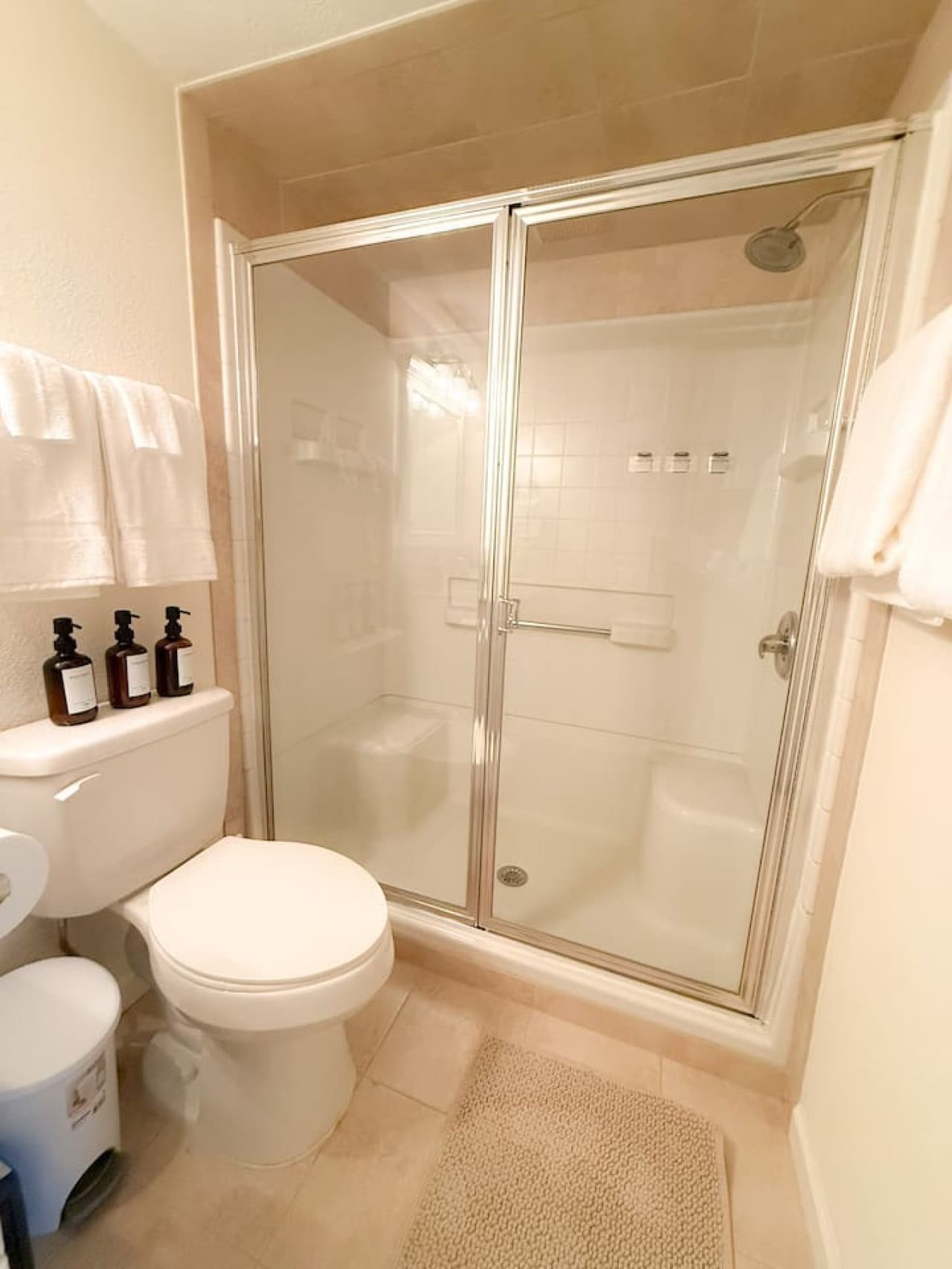 This well-maintained bathroom features a convenient walk-in shower with sliding glass doors and neutral-toned tile work. A clean white toilet and practical towel rack complete this efficient and tidy space.