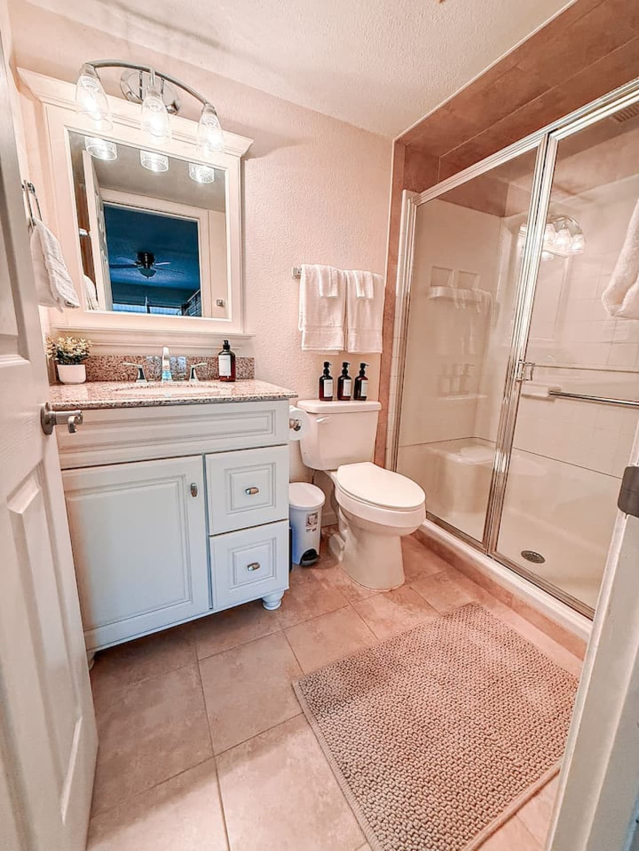 This well-appointed bathroom boasts a crisp white vanity with a granite countertop and ample storage, complemented by a large framed mirror with stylish lighting. A modern walk-in shower with sliding glass doors and neutral tiling creates a clean and