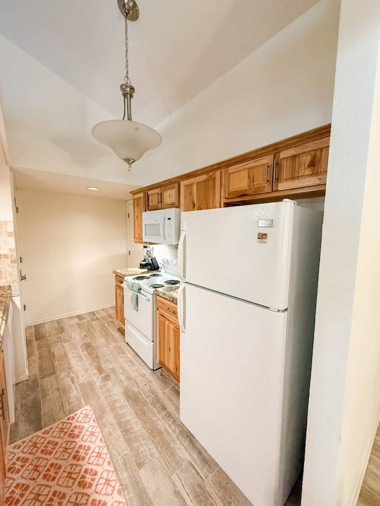 This efficient kitchen boasts warm wood cabinetry and a suite of white appliances, including a built-in microwave, offering both functionality and classic appeal. Durable wood-look flooring and a thoughtful layout make this a practical and inviting s