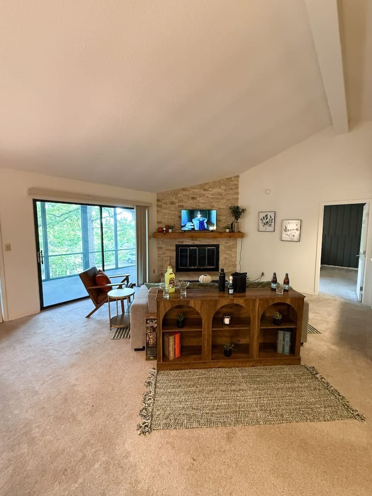 This inviting living room boasts vaulted ceilings and a cozy fireplace with a stone-accented hearth, perfect for relaxing evenings. Direct access to a screened patio extends the living space outdoors, while the open layout offers flexible furniture a