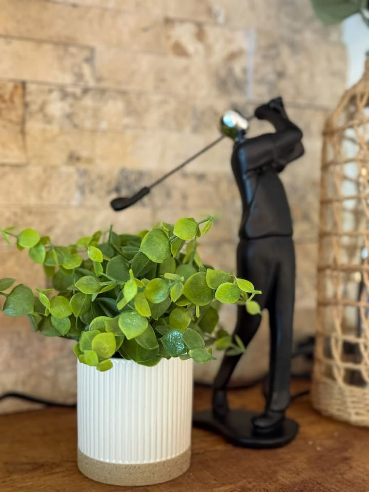 This delightful decorative vignette, featuring a vibrant faux plant in a stylish ribbed pot alongside a unique golfer figurine, adds a touch of personality and greenery. It subtly suggests a home that is thoughtfully decorated, offering both charm an