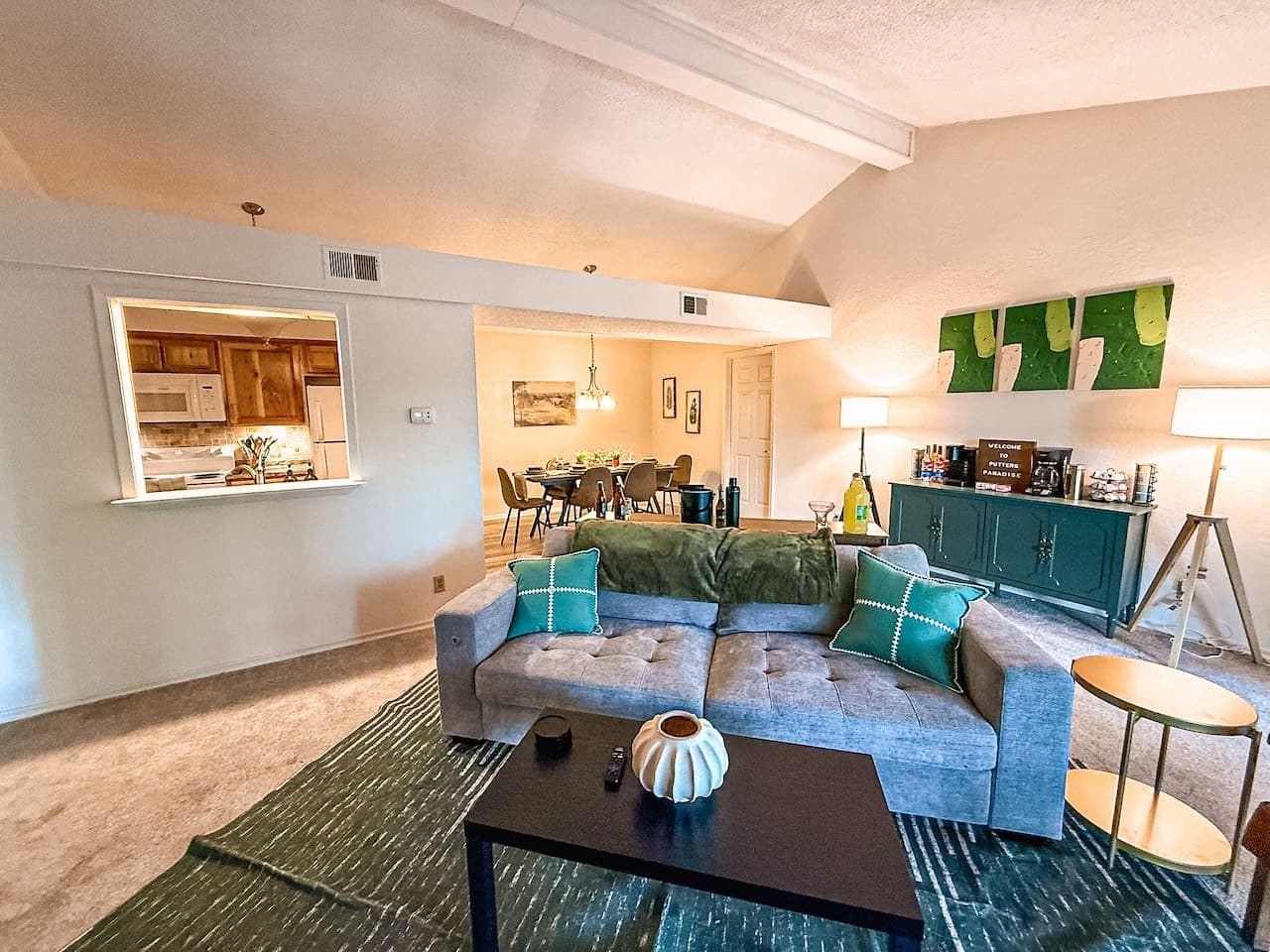 This spacious living room features vaulted ceilings, ample natural light, and an open pass-through to the kitchen, enhancing the sense of space and connectivity. The stylish decor and comfortable furnishings create a perfect environment for relaxatio