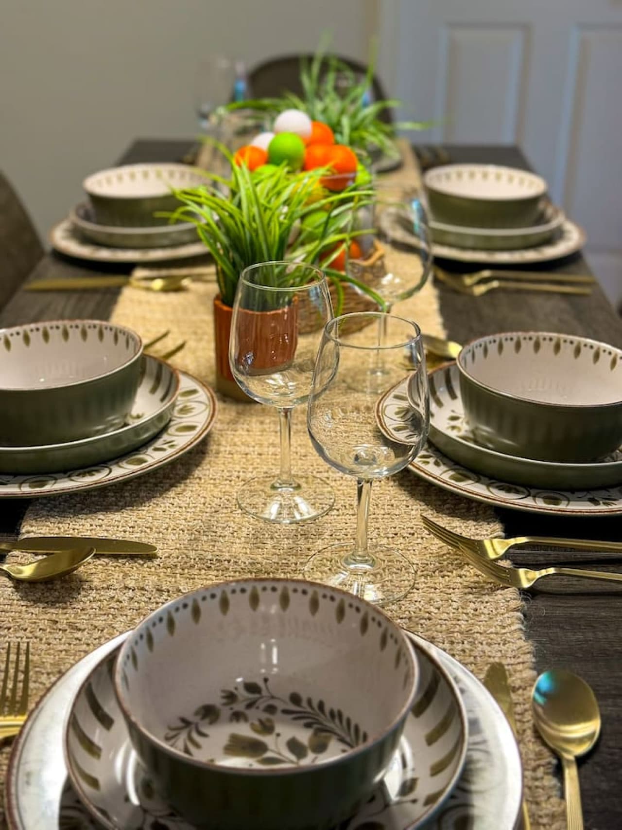The dining table is elegantly set with a golf-themed centerpiece featuring colorful practice golf balls in a clear vase nestled within a wicker basket, complemented by small potted plants. Each place setting includes stylish dinnerware, wine glasses,