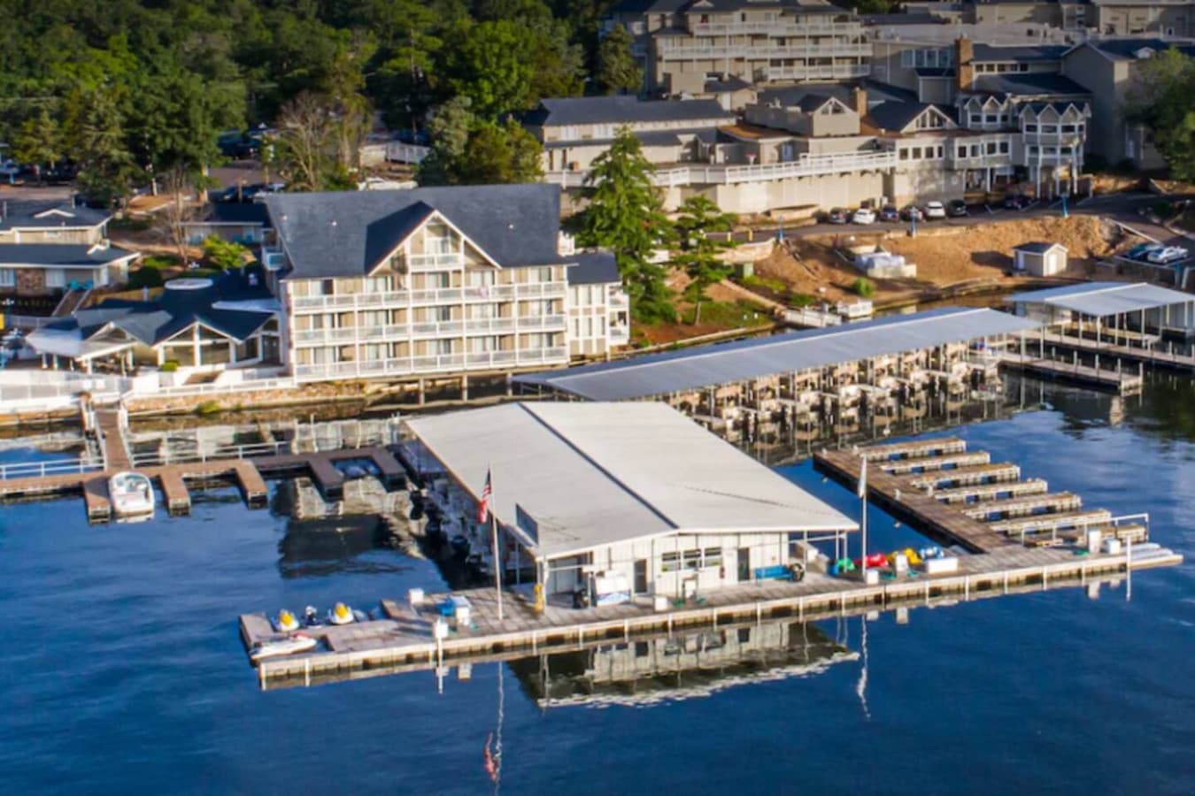 This stunning aerial view showcases a vibrant waterfront resort property, complete with extensive docking facilities for boats and a sparkling lakeside pool area. Numerous buildings, including multi-story accommodations, are nestled among lush greene