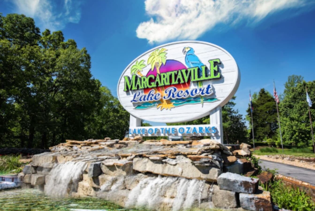 This welcoming entrance features the Margaritaville Lake Resort sign, set against a backdrop of lush greenery and a cascading water feature. The vibrant colors and inviting atmosphere suggest a relaxing and enjoyable vacation destination.