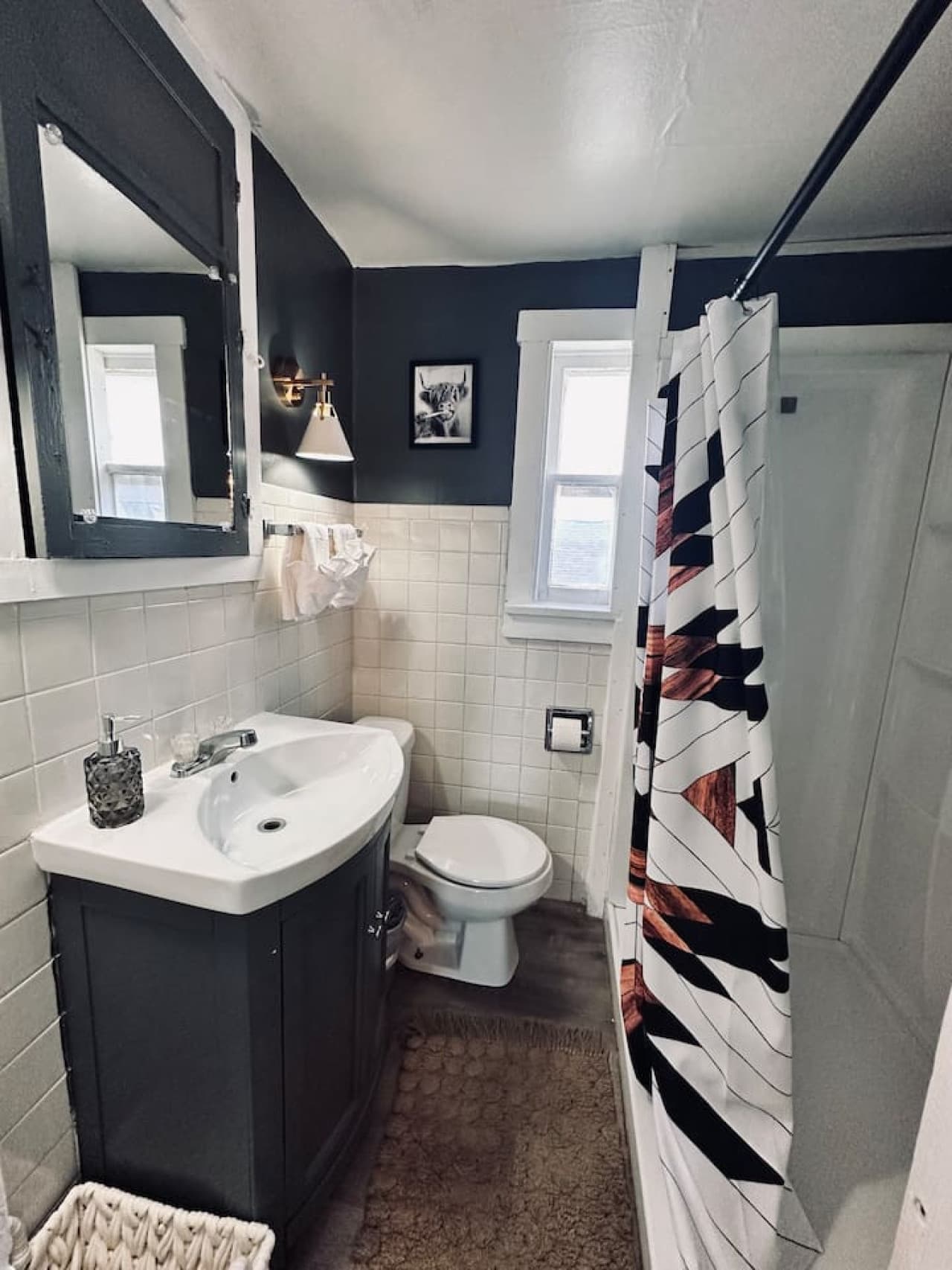 This well-maintained bathroom features a modern toilet and a practical shower-over-tub setup, perfect for both quick rinses and relaxing soaks. The thoughtful inclusion of wall-mounted shelving above the toilet offers convenient storage, enhancing th