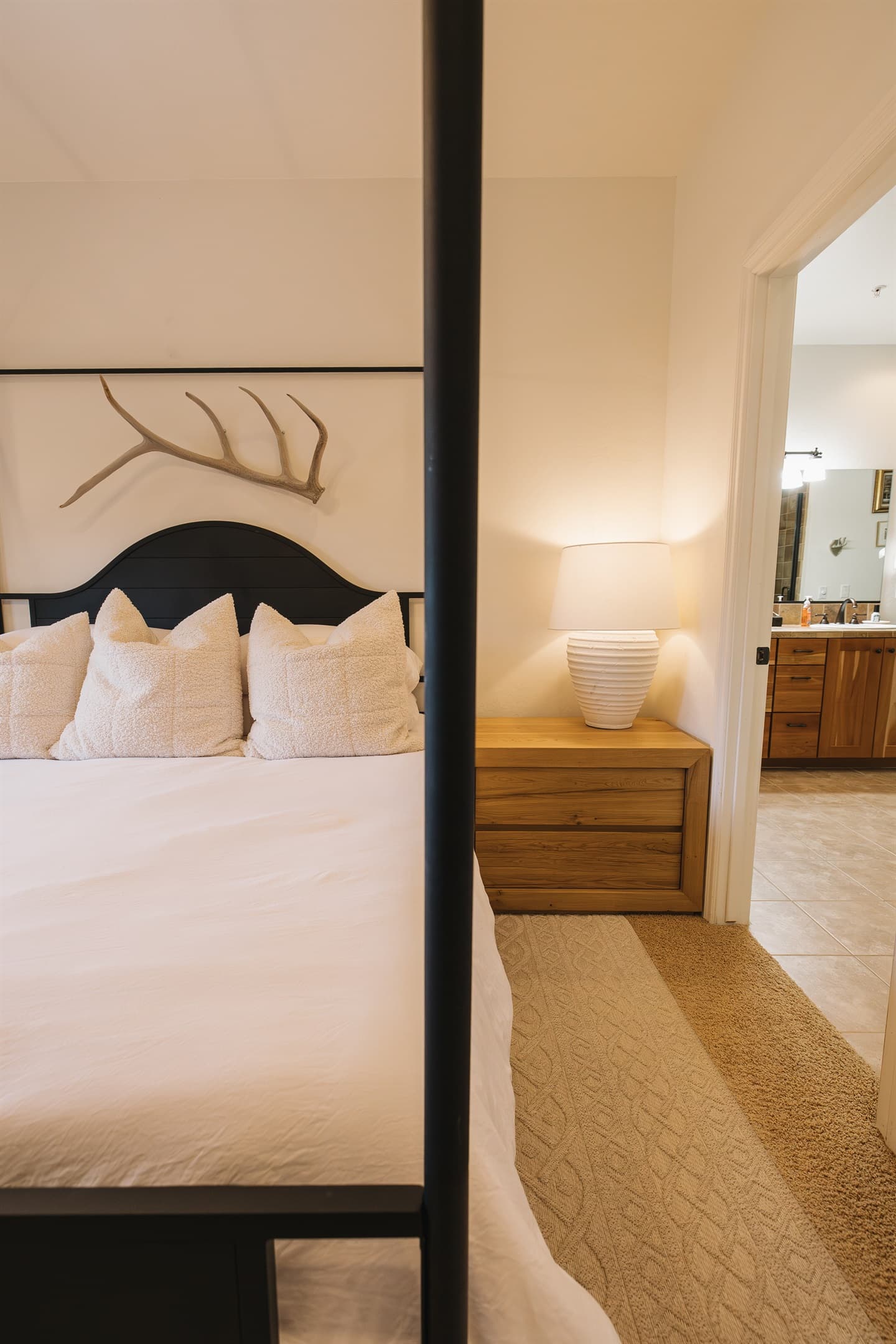 A serene primary suite designed for rest and retreat. Crisp white linens, plush textured pillows, and a statement four-poster bed create a cozy yet refined mountain feel. The private ensuite bathroom is just steps away, offering seamless comfort and conven