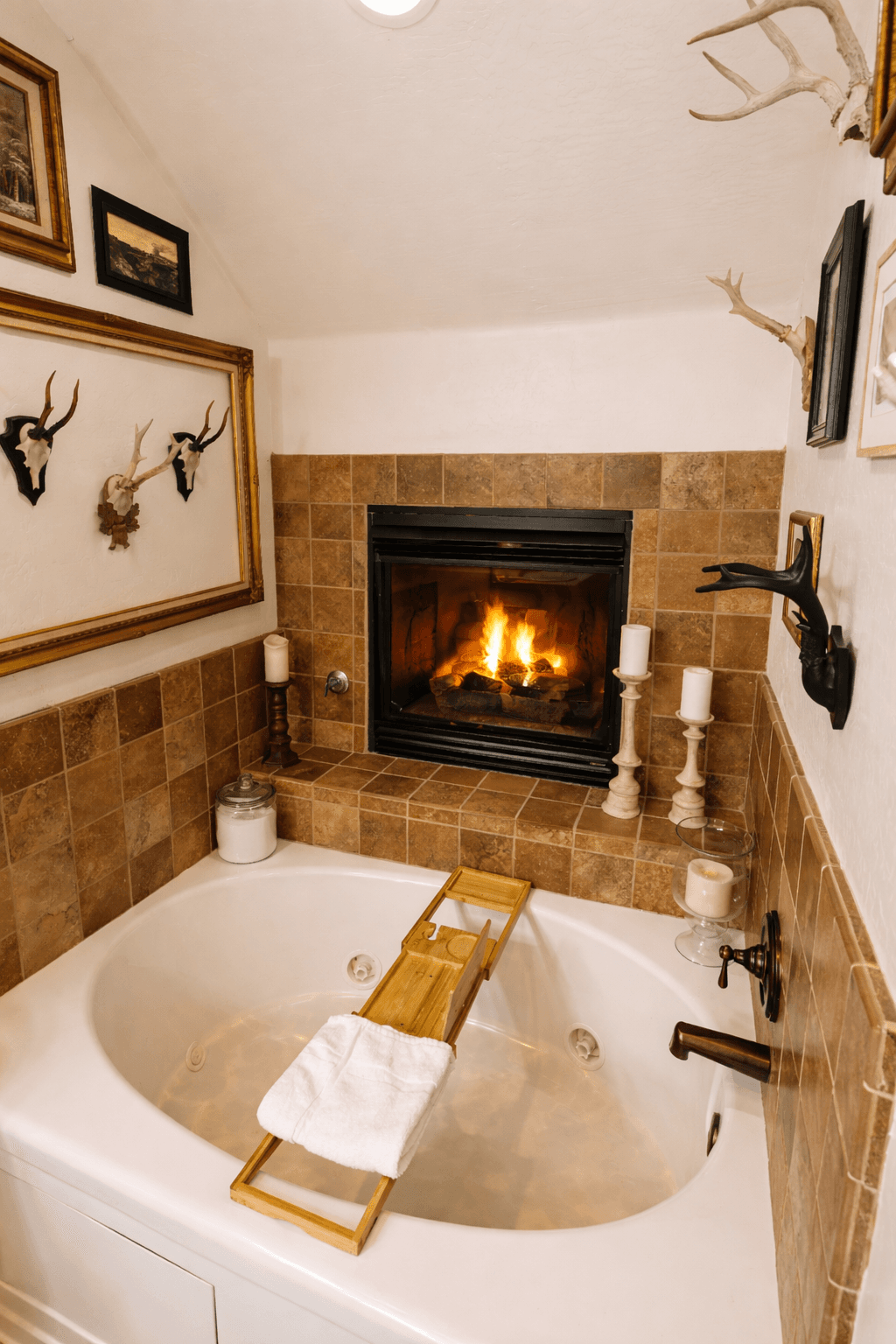 Luxuriate in a spa-like soaking tub beneath a glowing gas fireplace. This serene bathroom retreat features a deep jetted tub, warm stone tile, plush towels, and curated décor—perfect for unwinding after mountain adventures with a glass of wine and total re