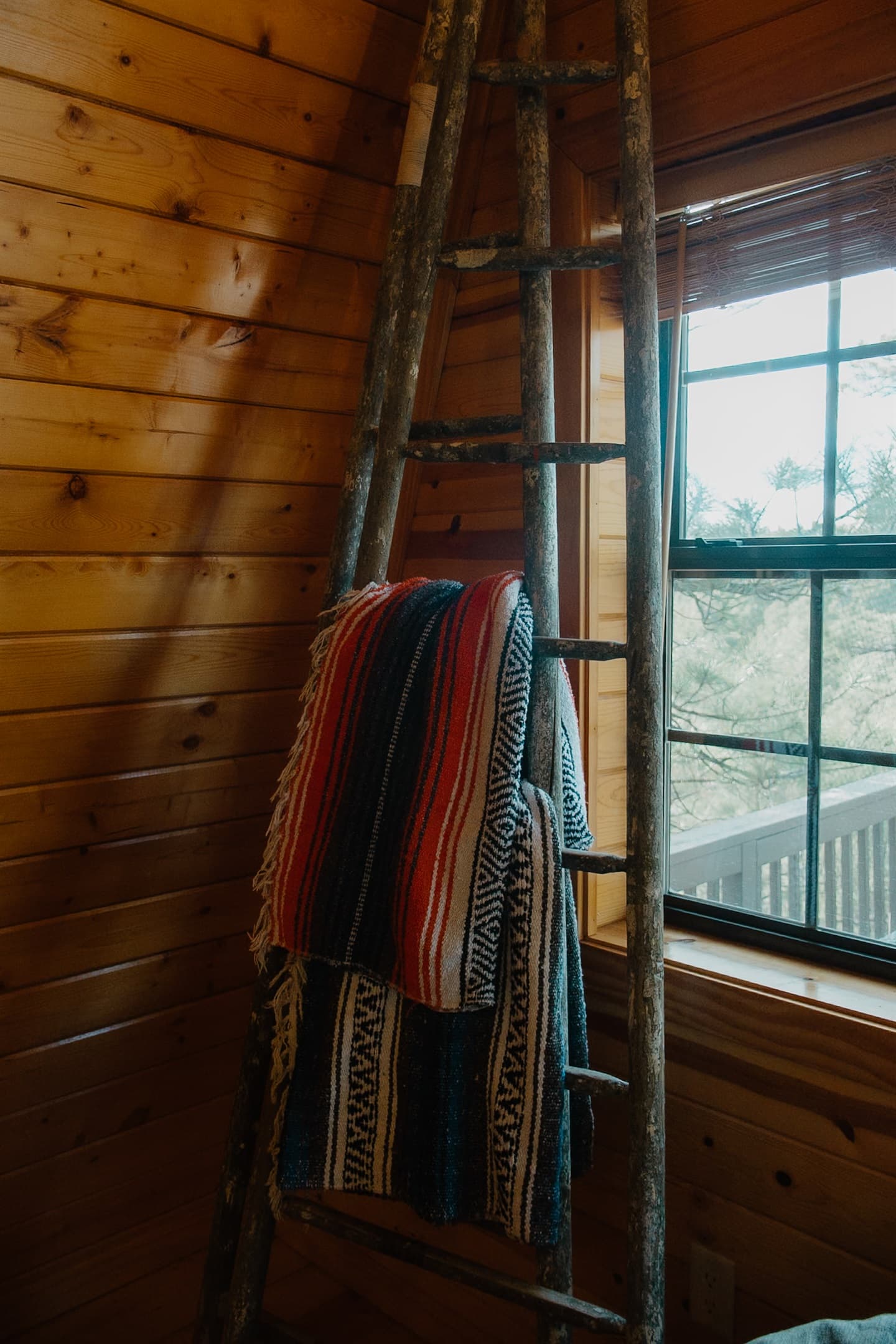 Rustic A-frame charm meets mountain views with this cozy ladder nook and natural wood interior. Sunlight pours in through the window, highlighting the cabin’s warm, inviting design in Arizona’s White Mountains.
