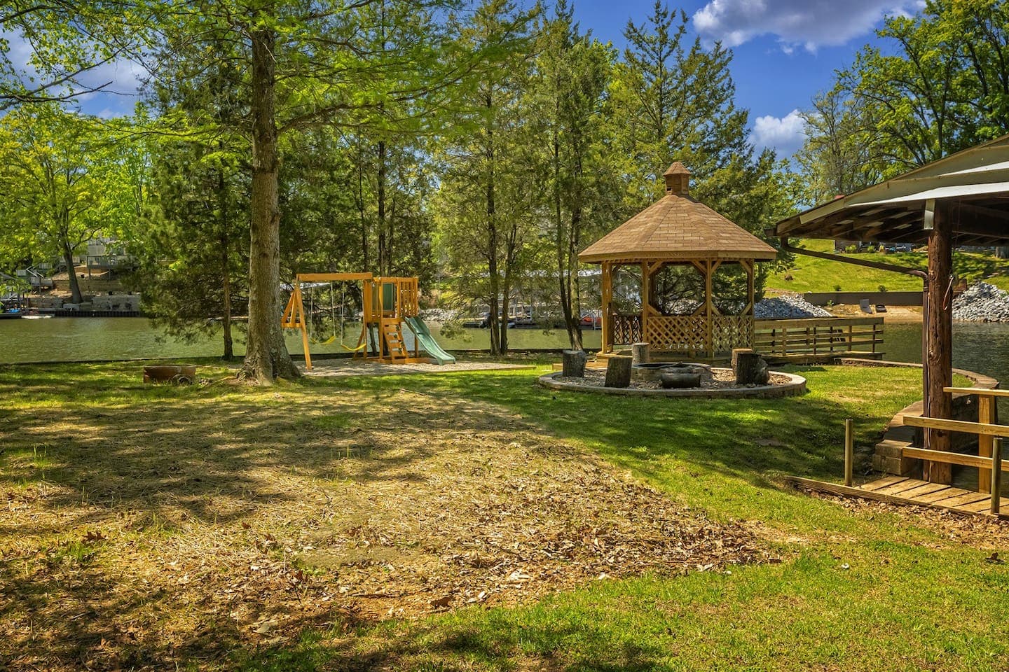 A beautiful gazebo and swing set in a house's yard.