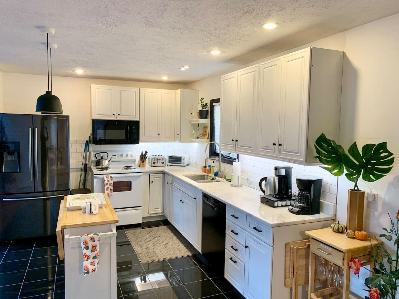 A large modern kitchen of black and white with granite counters, a large fridge, a coffee station, and a center island. All items are labeled for your convenience. 