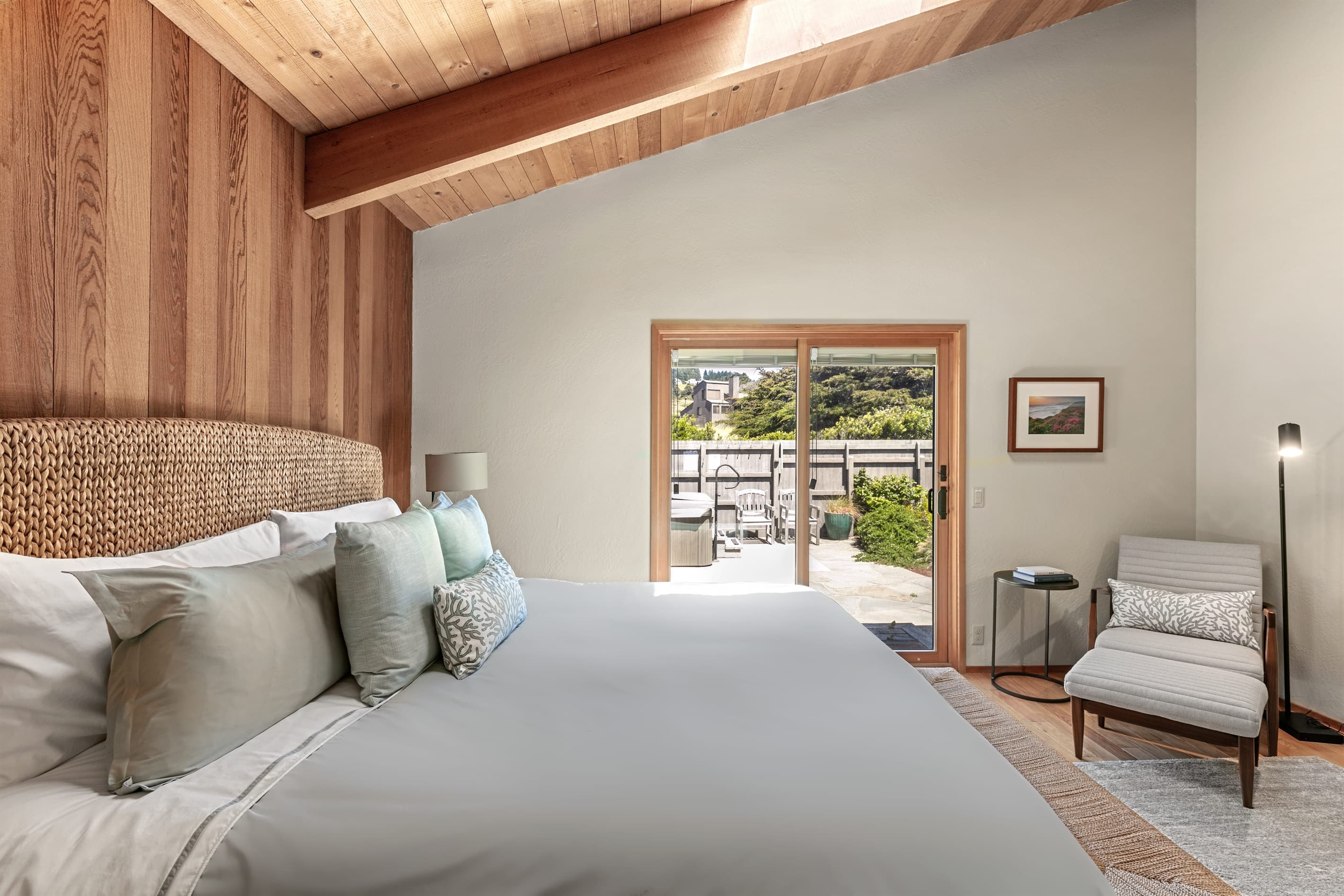 At night, softened light settles over natural wood and a seagrass headboard, while a skylight above opens the room to stars and passing clouds—an intimate connection to sky, sea, and quiet.