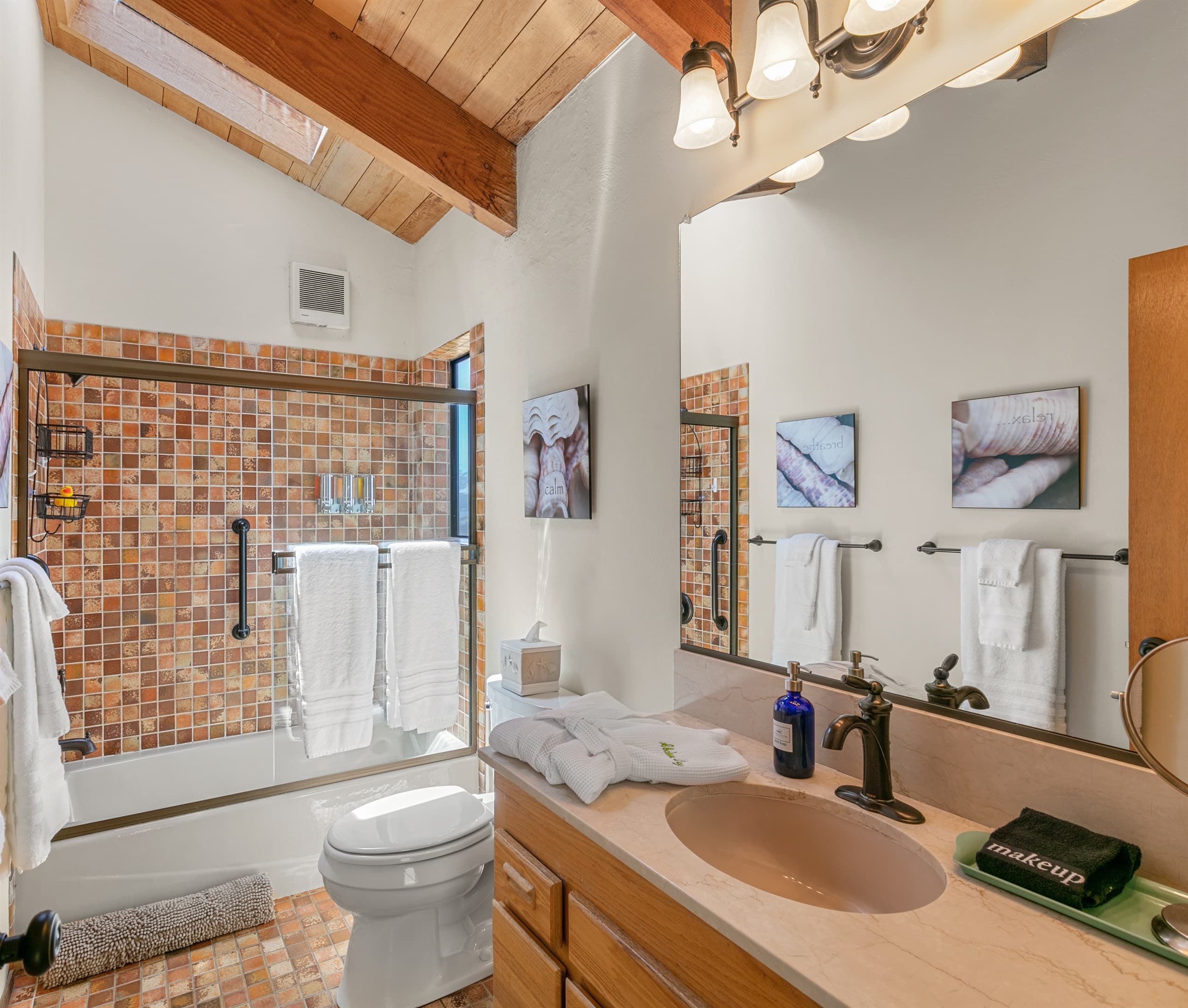 Spa-inspired comfort meets rustic elegance: This sunlit bathroom features plush towels and thoughtful details, creating a serene and refined retreat for your coastal escape.