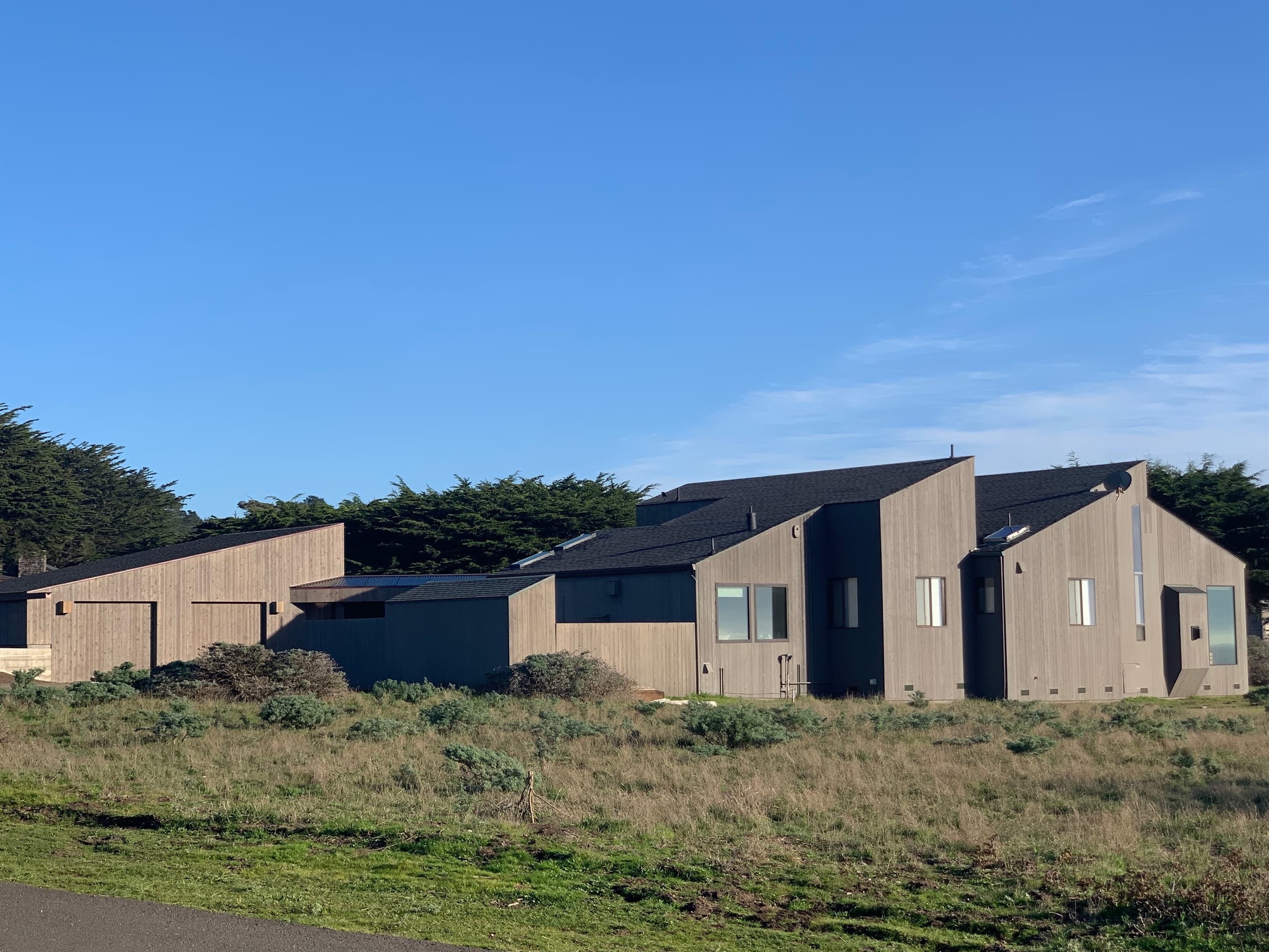 Full west-side view showcasing the sleek sawtooth architectural design of this ranch style Sea Ranch retreat and detached garage—an elegant blend of coastal living and modern design.