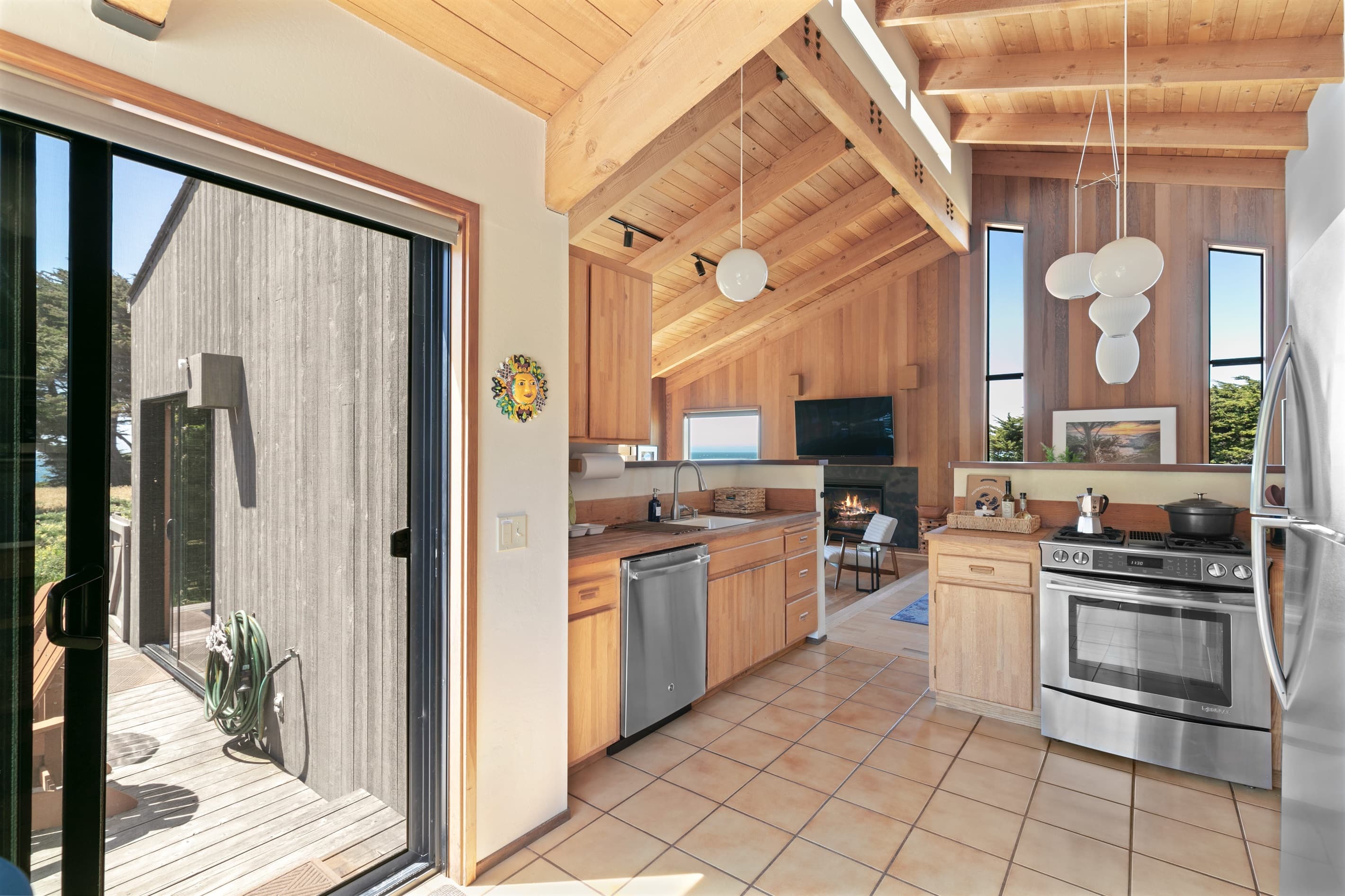 Sophisticated coastal living: This sunlit kitchen blends sleek stainless steel appliances with natural wood finishes, soaring ceilings, and effortless indoor-outdoor flow—perfect for refined gatherings and gourmet moments by the sea.