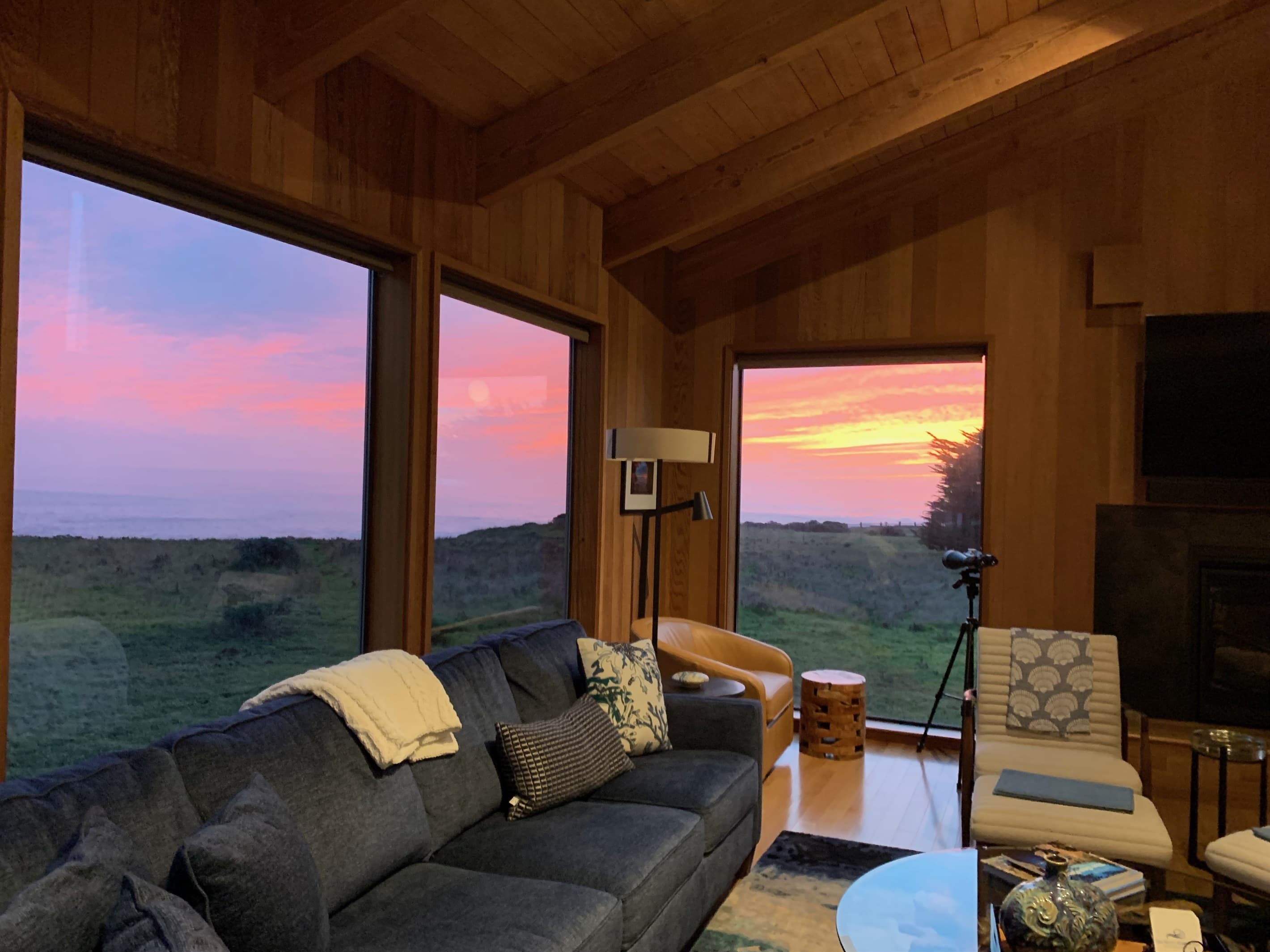 Warm winter sunset glows through expansive ocean-view windows, casting a golden-pink hue across this elegant living room—where refined coastal comfort meets nature’s seasonal splendor. 
