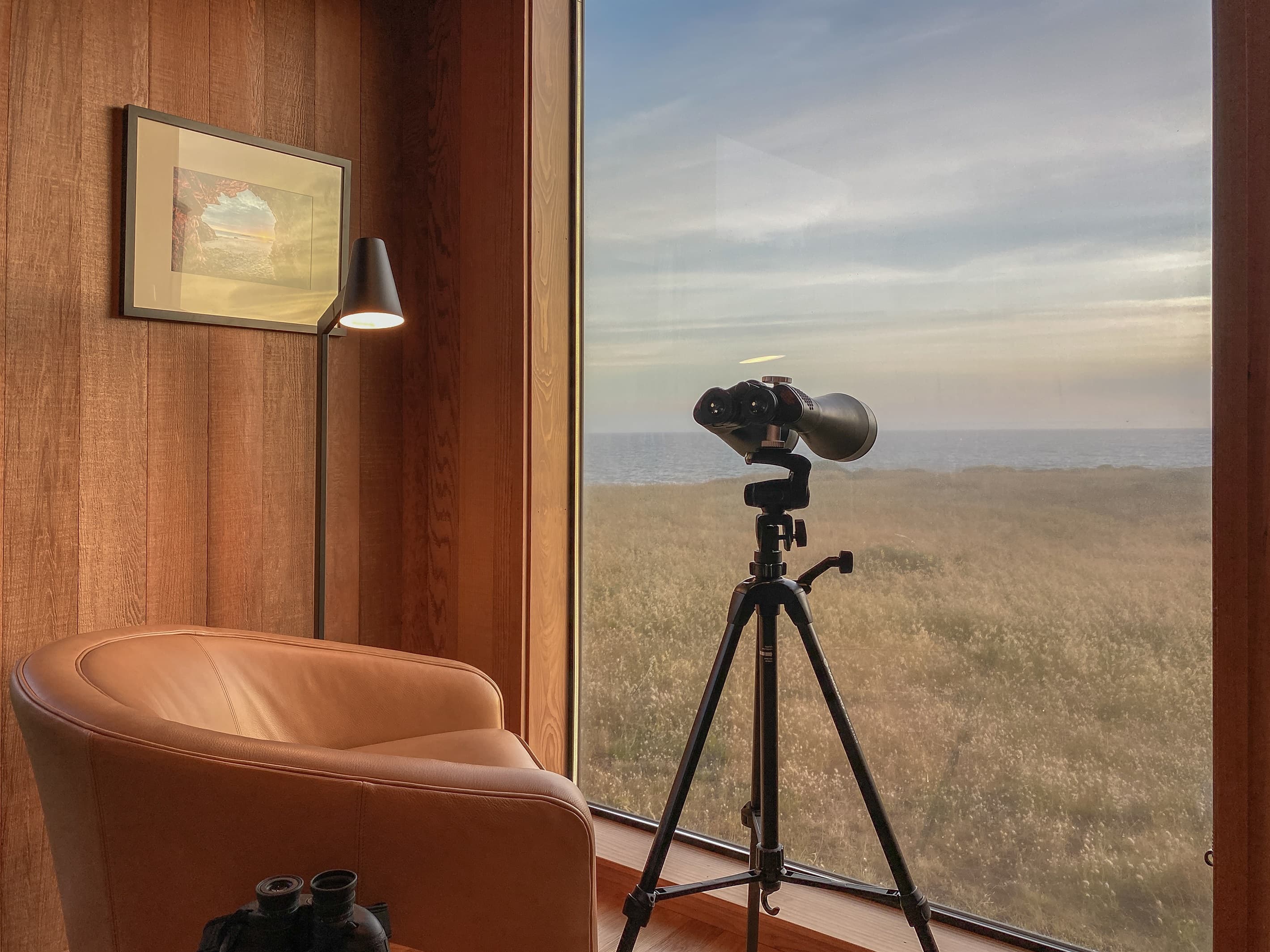 Golden hour tranquility: A leather chair, floor lamp, and mounted binoculars create a refined coastal observatory. Savor ocean views, stargazing, or spotting whales from the comfort of your private retreat. 