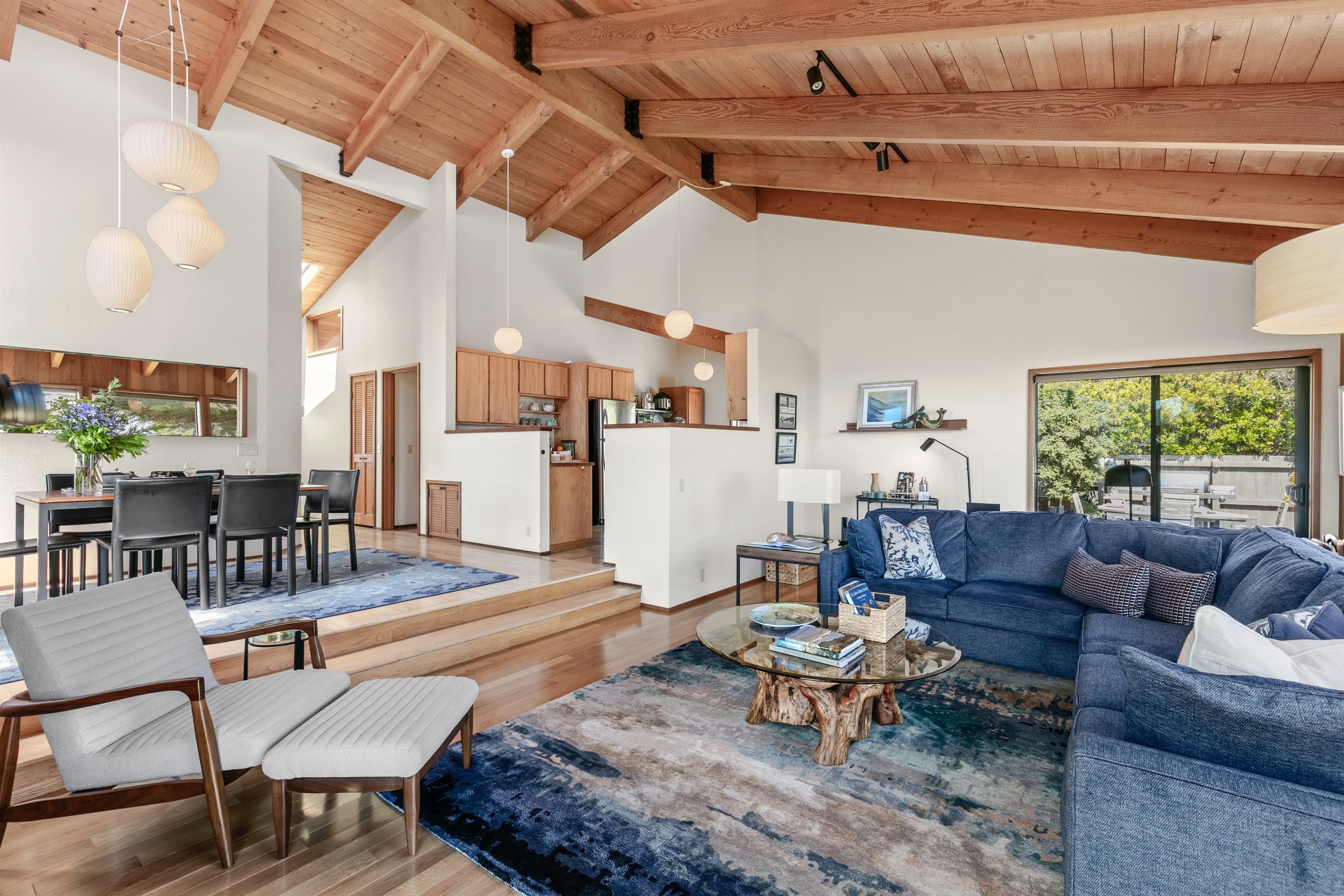 Open-concept elegance with vaulted ceilings, coastal blue accents, and layered rugs throughout the living, dining, and kitchen areas—designed for relaxed sophistication with ocean views from every angle. 