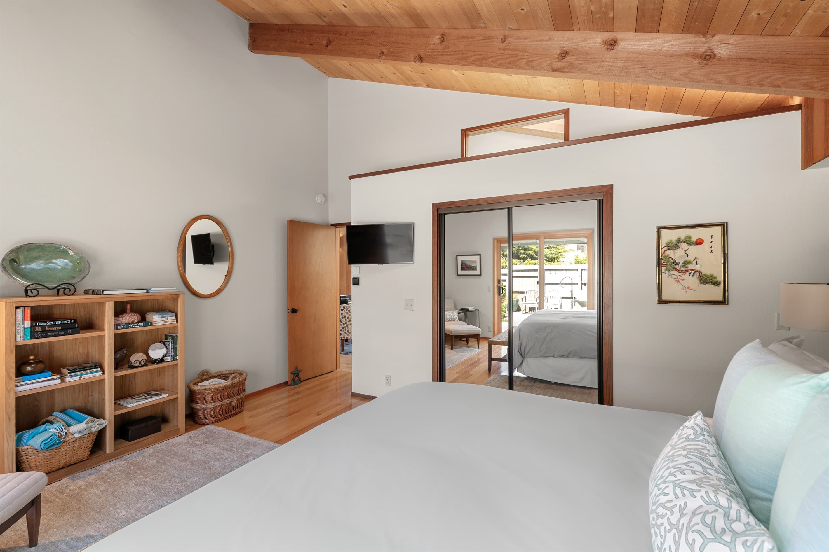 Light-filled principal bedroom blends iconic Sea Ranch architecture with relaxed luxury. Vaulted wood ceilings, skylight, with blinds, curated books, and plush bedding invite you to unwind in timeless coastal elegance.