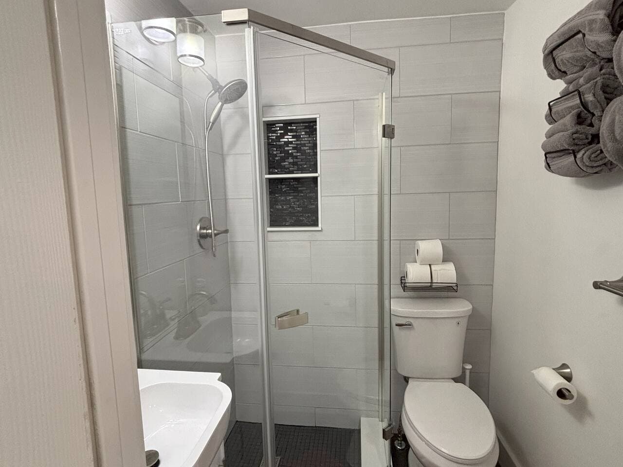 The compact bathroom has a custom built glass shower enclosure, single bowl vanity, and storage for supplies and linens.  