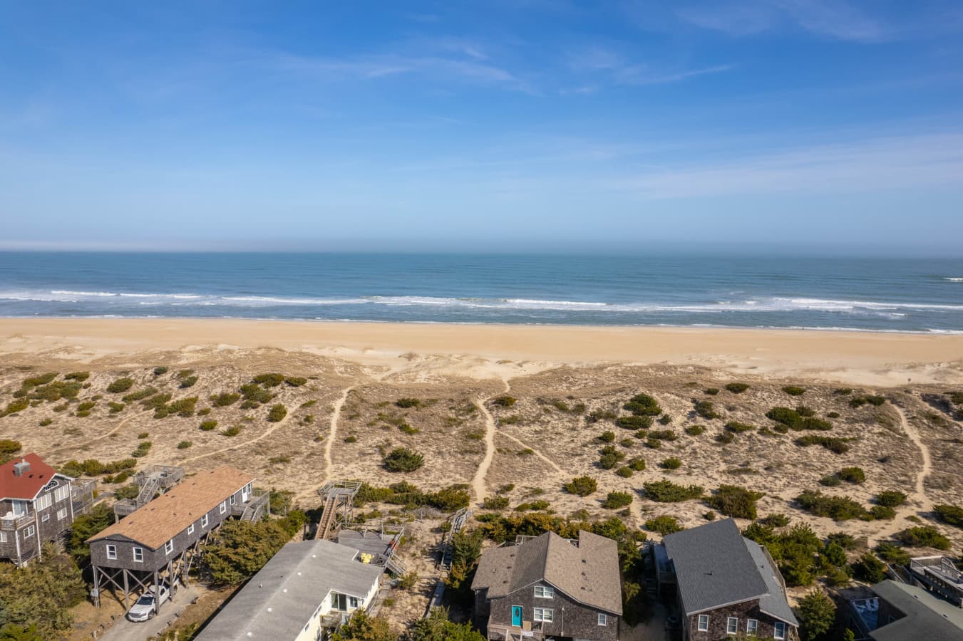 Aerial over the neighborhood w/ the dune field & ocean surf beyond the rooftops.