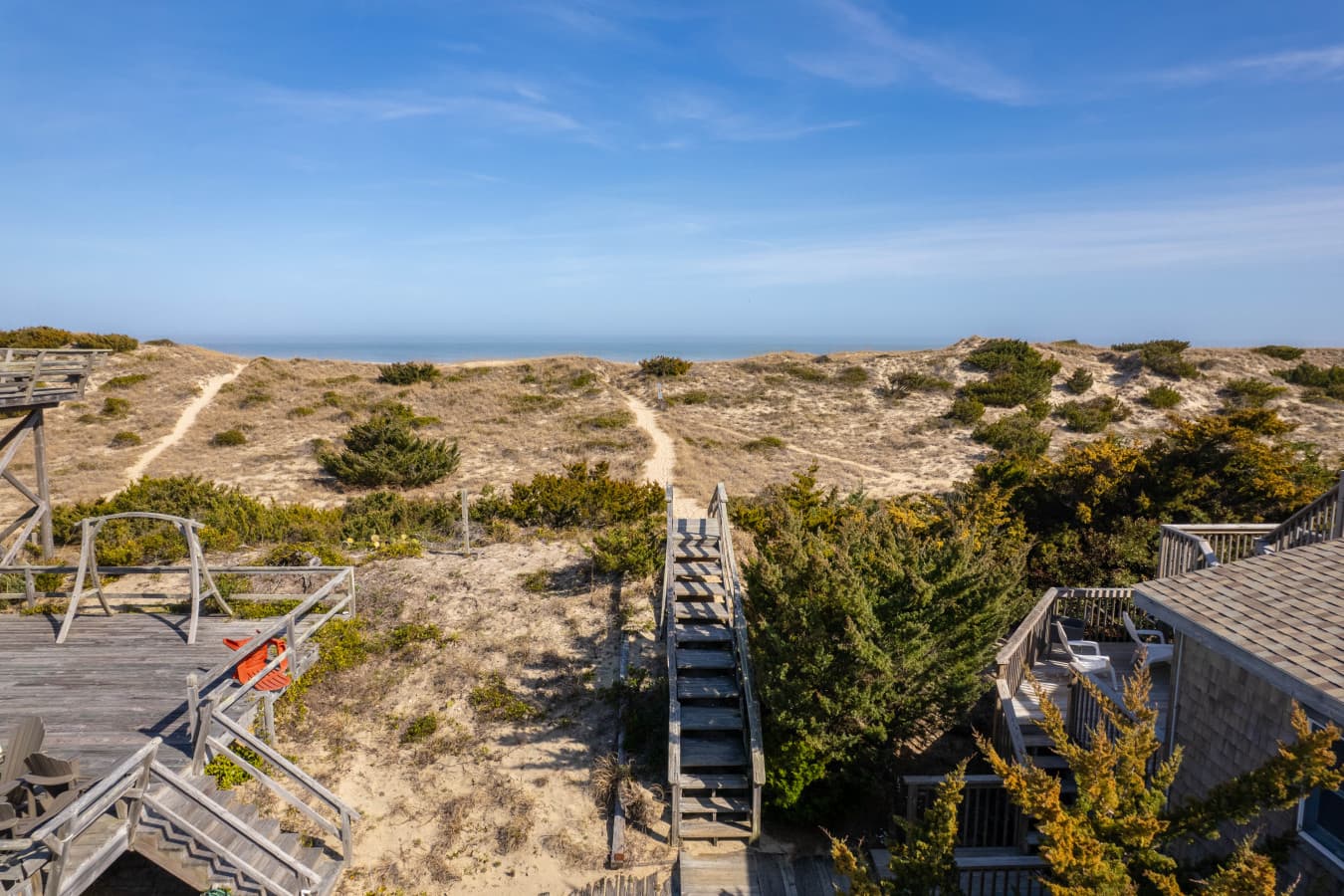 Deck view over the dune field w/ wooden steps, sand footpaths & the ocean on the horizon.