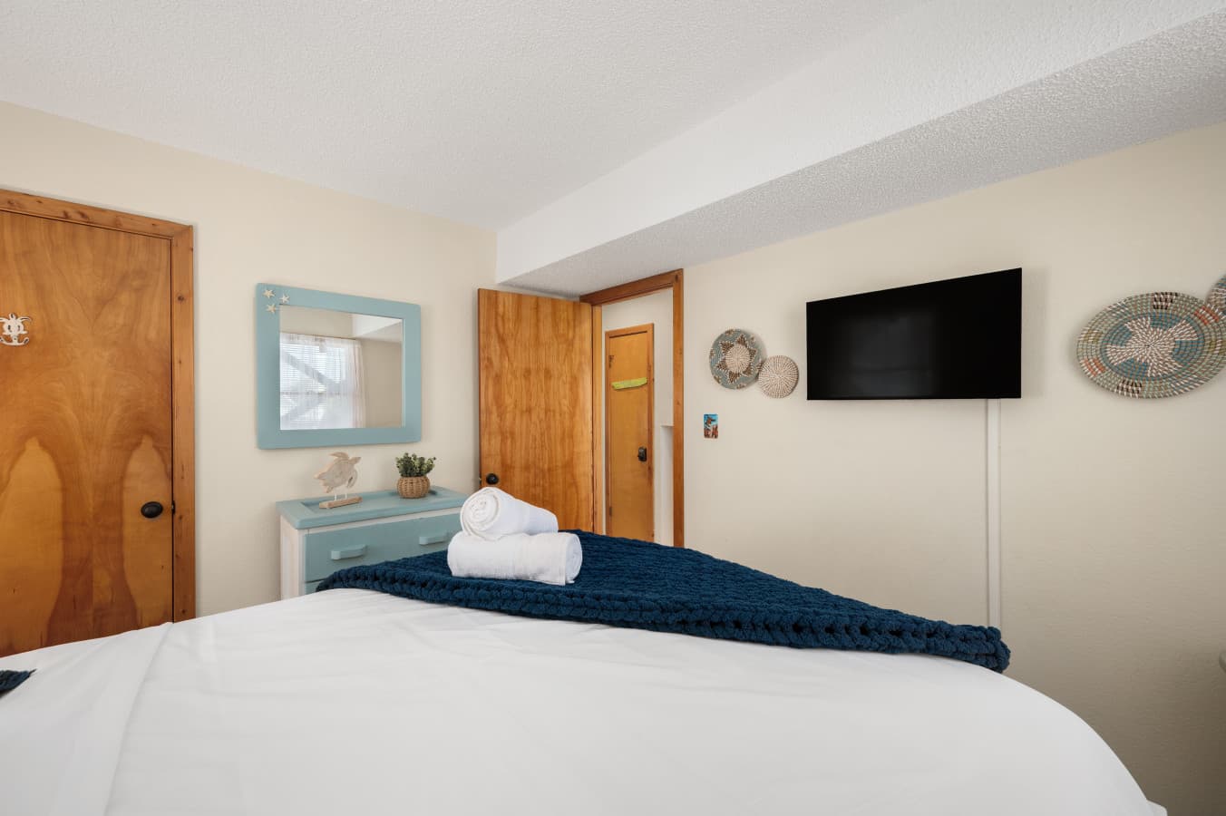 Cozy bedroom w/ soft bedding, wall-mounted TV & warm wood accents