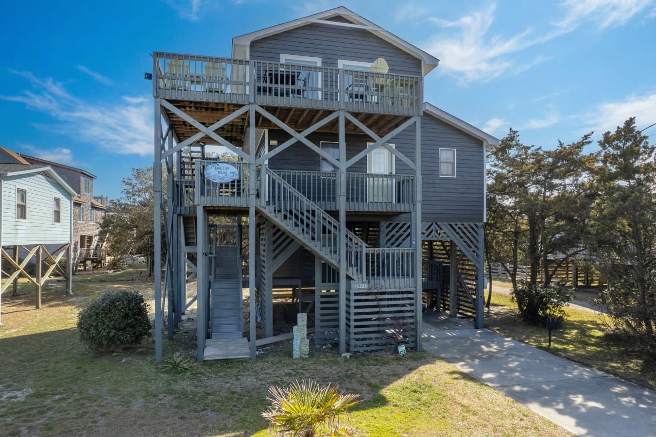 Elevated coastal home w/ wraparound decks & exterior stairs surrounded by trees