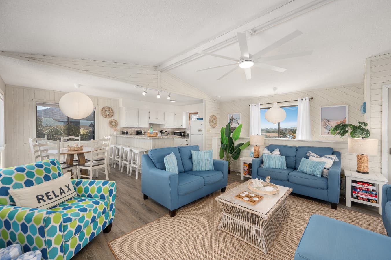 Open living, dining & kitchen under a vaulted plank ceiling w/ soft blue seating for the group.