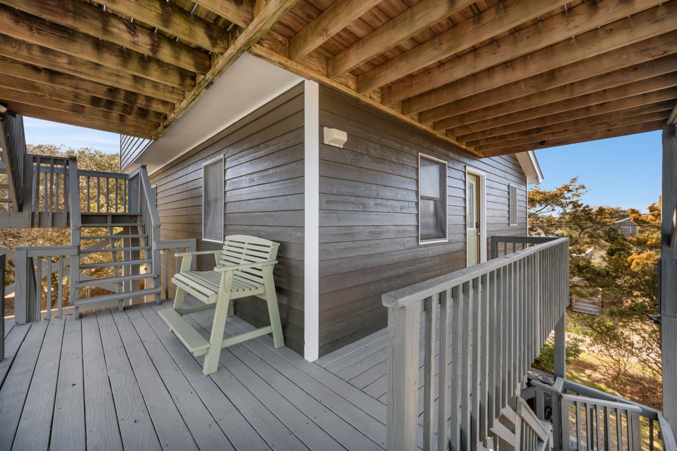 Covered deck under the upper level w/ a chair & rail looking out over the dune shrubs.