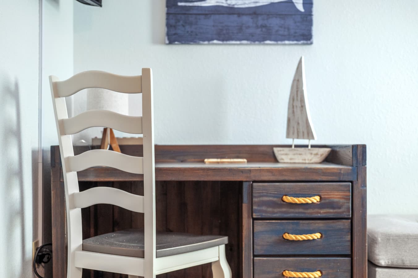 Wood desk w/ rope-pull drawers, ladder-back chair & a sailboat accent for a quiet work spot.
