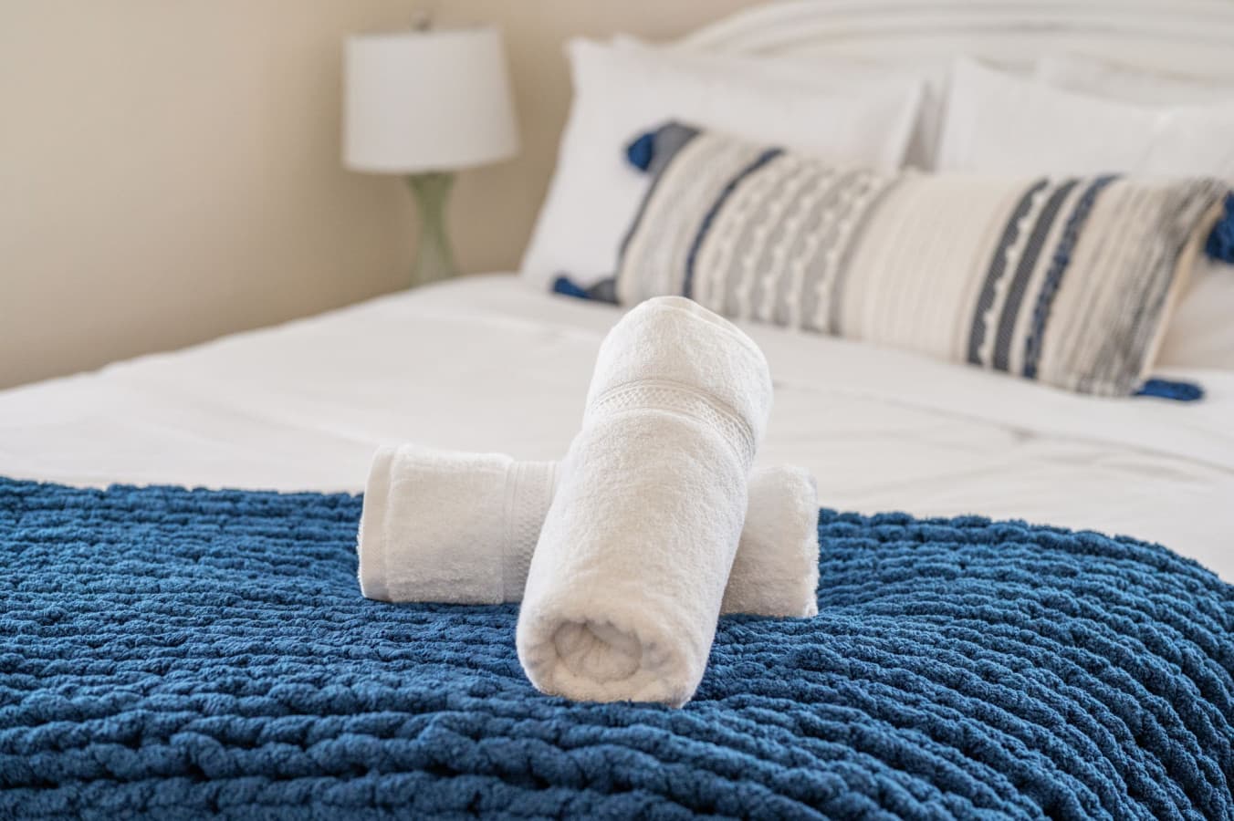 Bed detail w/ crisp white linens, a chunky navy knit throw & fresh rolled towels set out.