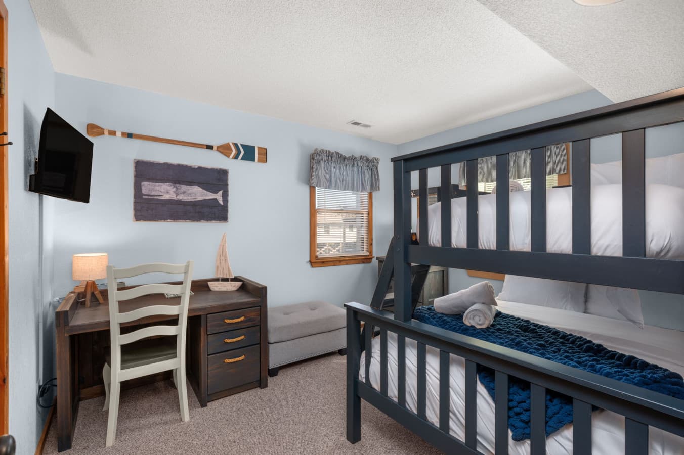 Bedroom w/ bunk beds, a desk and chair, wall-mounted TV & nautical oar decor.